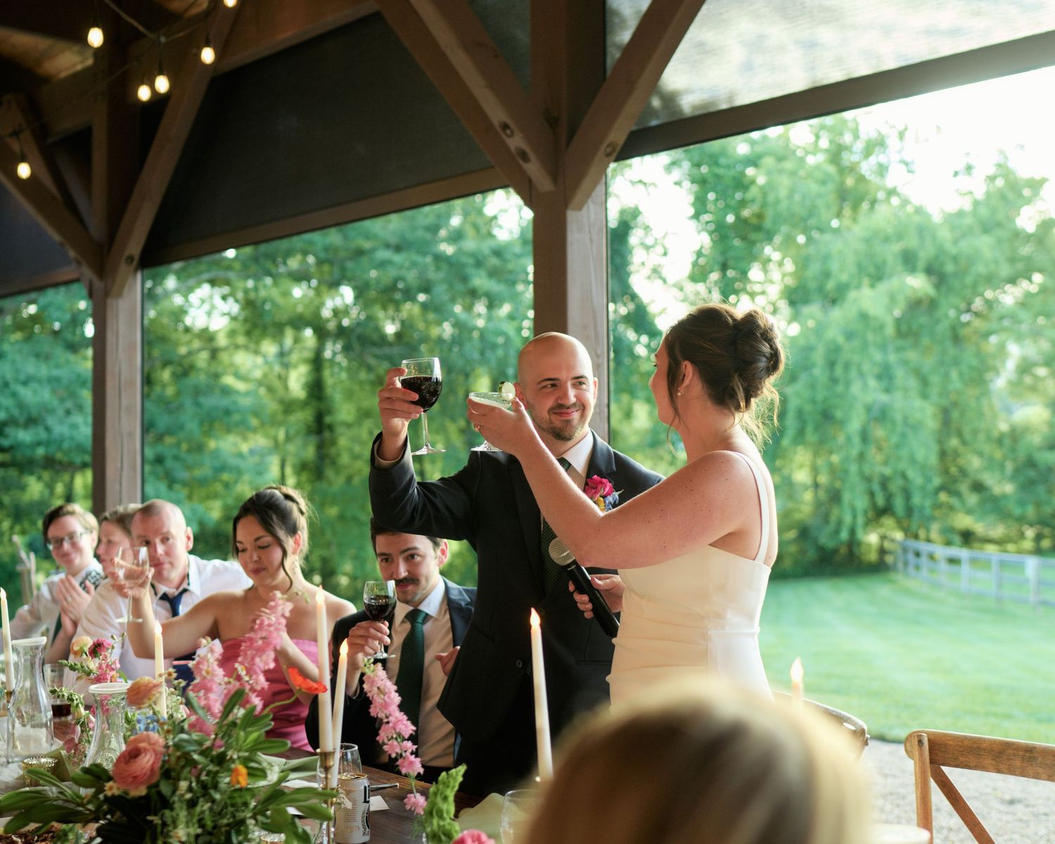 Wedding reception celebration with toasts and floral decorations under a covered pavilion.