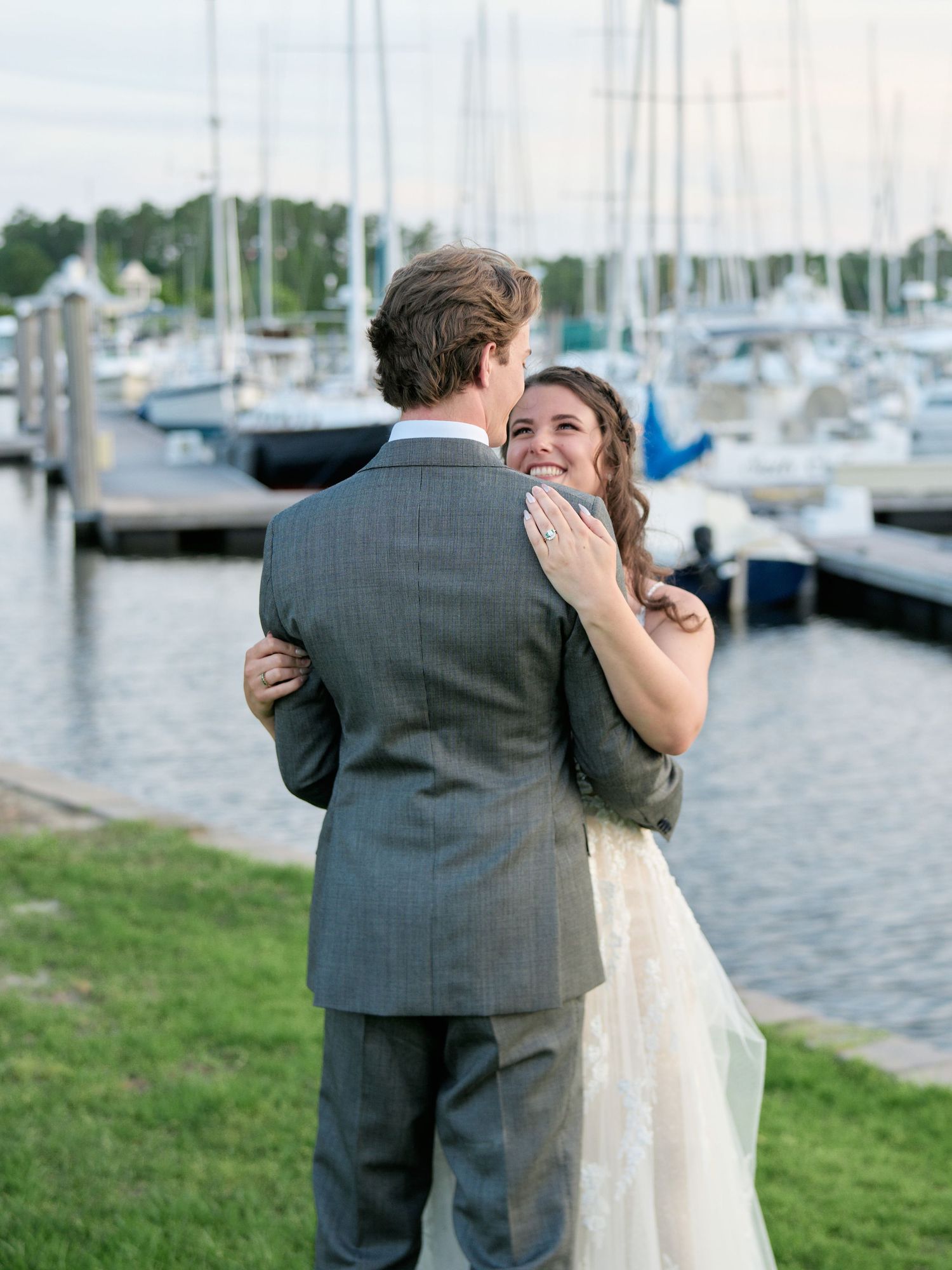A romantic moment between a couple by the marina with sailboats and water in the background.