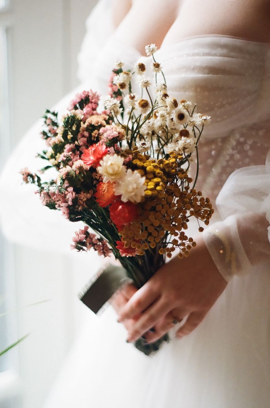 A delicate bridal bouquet with pink and white dried flowers held against a white dress.