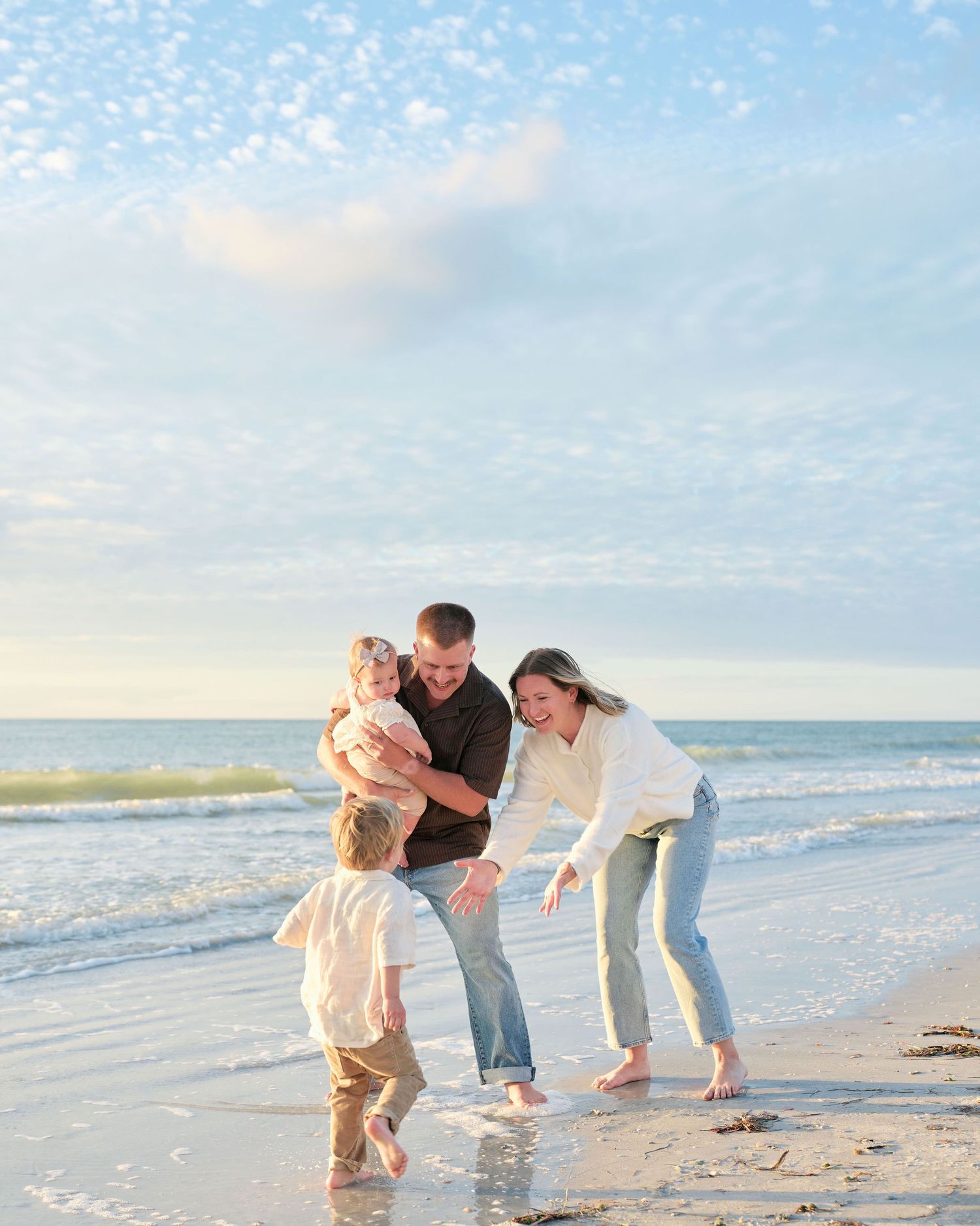 A family plays together on a sunny beach with waves and blue sky in the background.