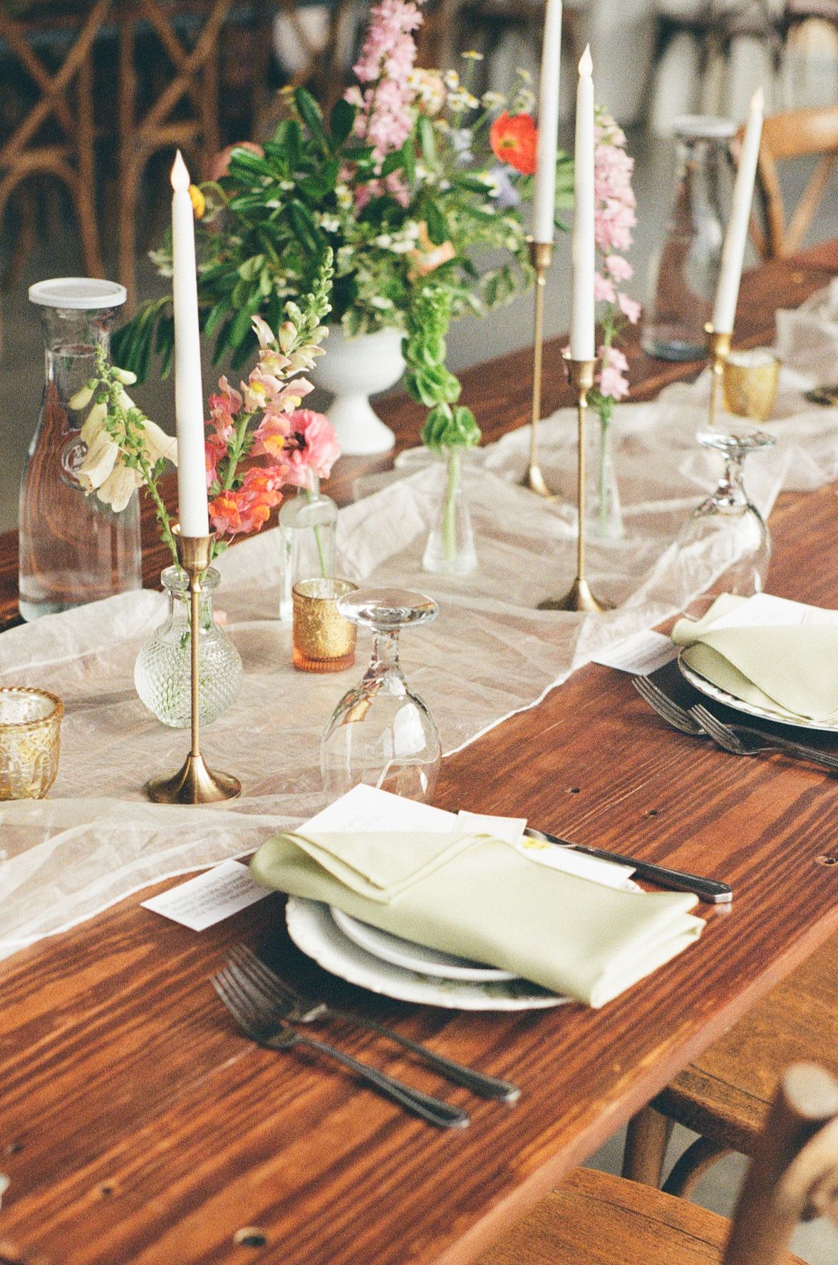 Elegant table setting with white candles, delicate pink flowers, and rustic wooden table for a romantic dinner party.