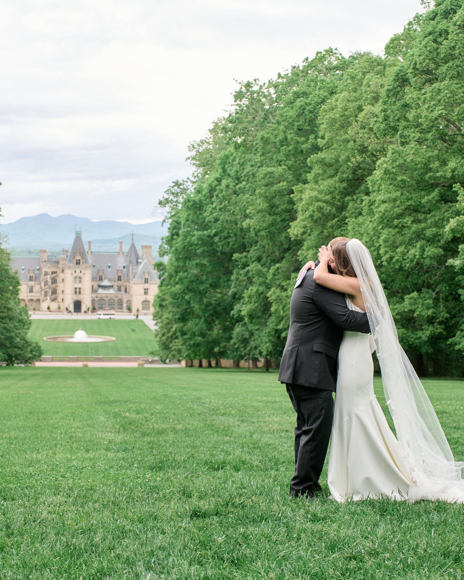 A couple shares an intimate moment on the expansive green lawn with a majestic castle in the background.