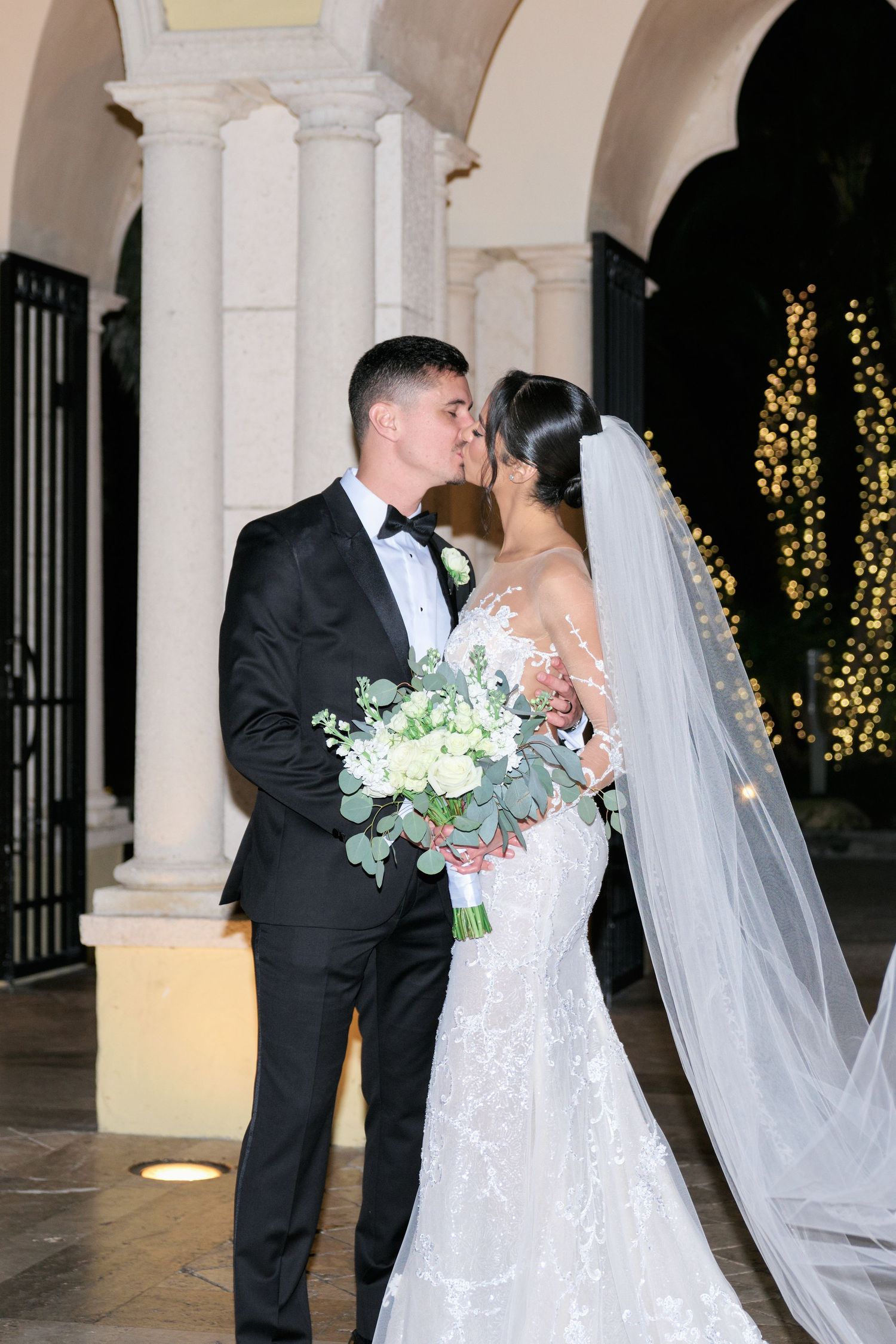 Romantic wedding portrait of couple embracing under arched columns with bouquet.