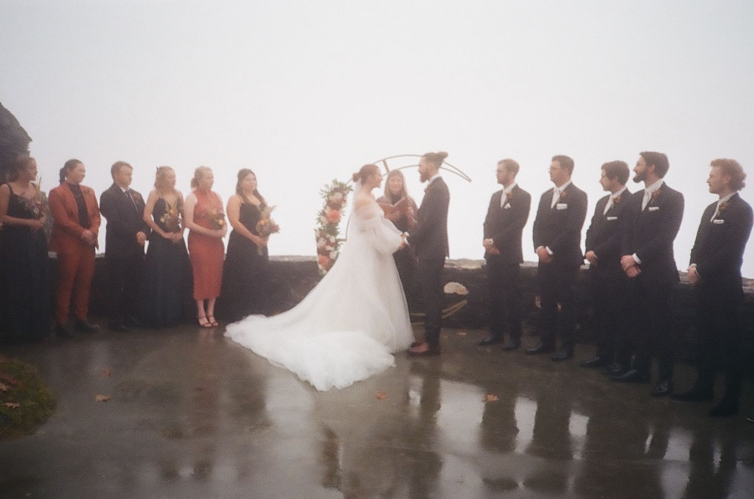 Wedding ceremony silhouette with bridal party and guests gathered in misty outdoor setting.