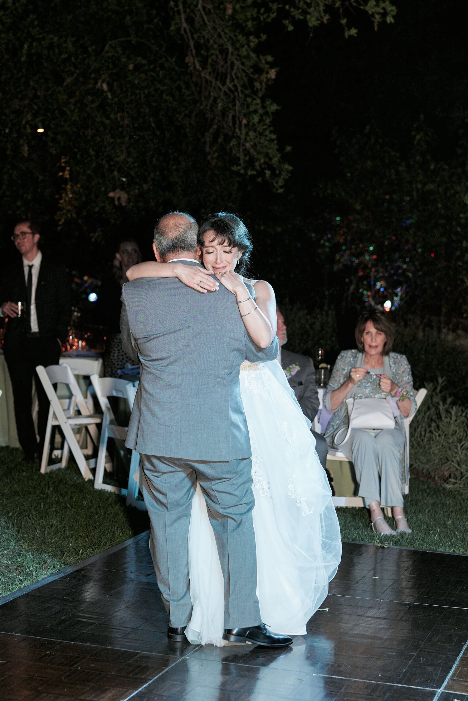 A couple shares an intimate dance together at an outdoor evening wedding reception on a dark dance floor.