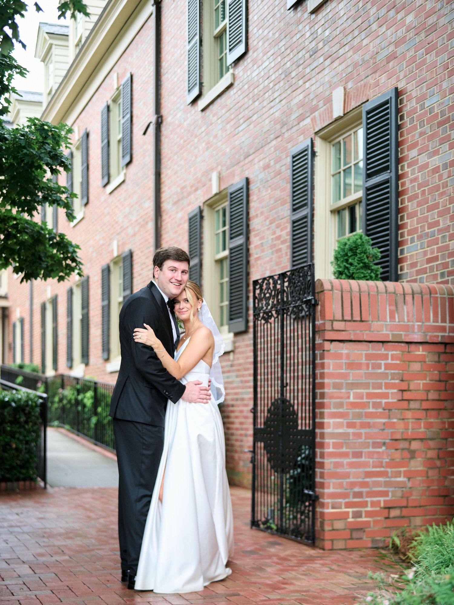 Elegant wedding couple embraces against a classic brick building backdrop.