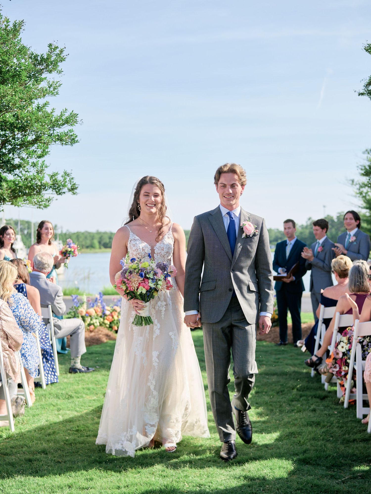 A couple walking down the aisle at an outdoor wedding ceremony on a grassy lawn with guests seated on either side.