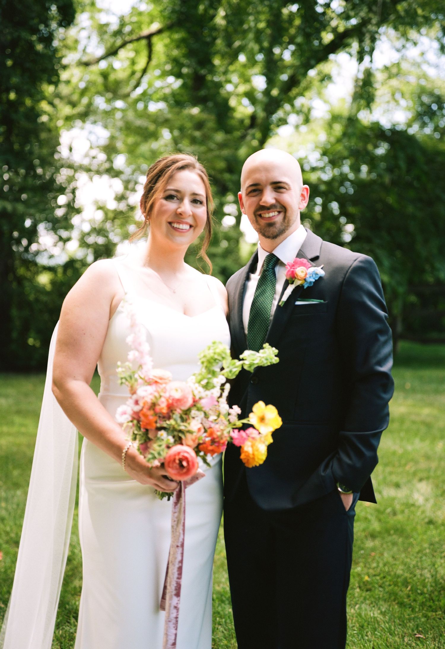 A joyful wedding portrait with colorful bouquet in a garden setting.