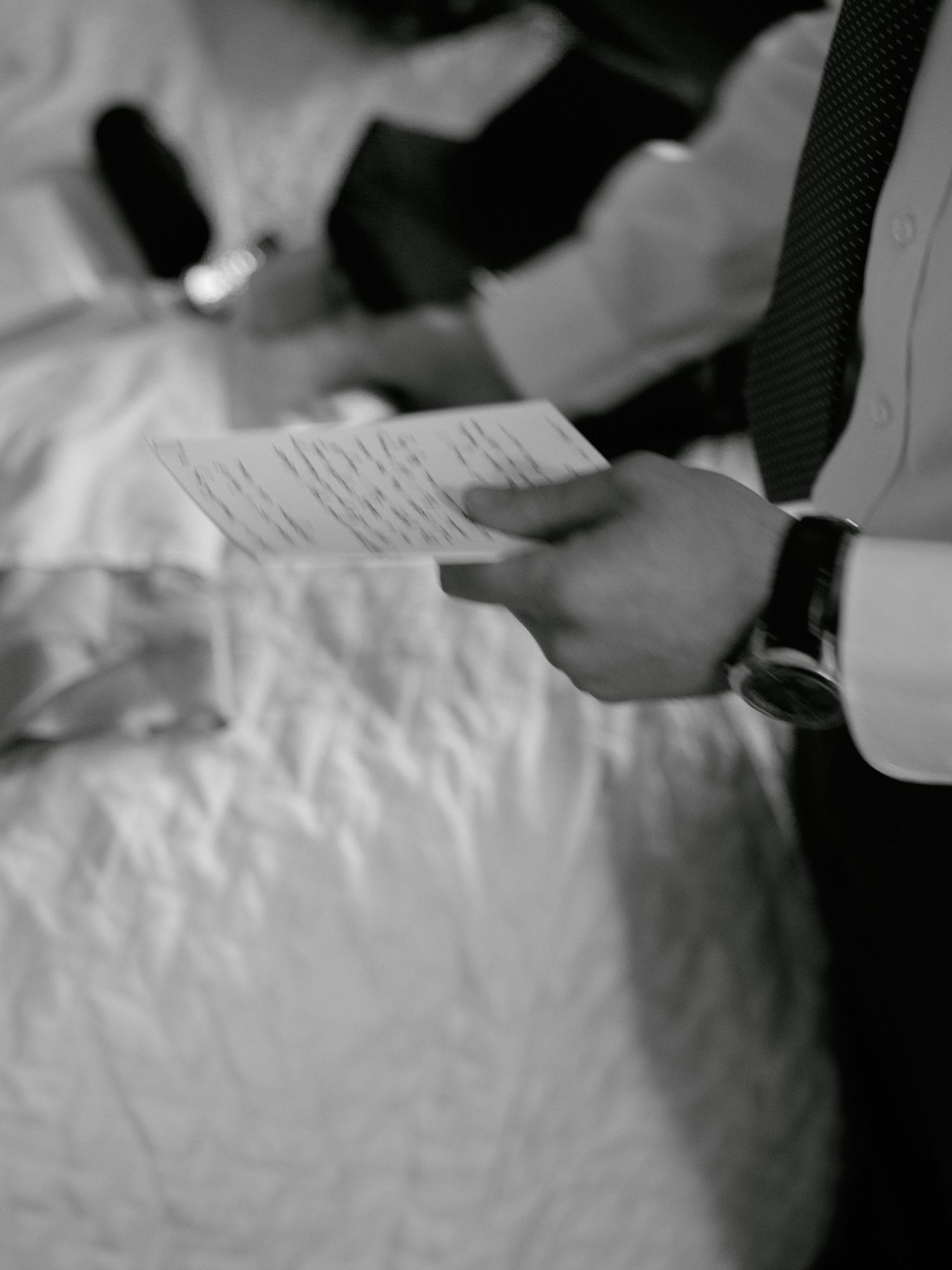 Black and white close-up of hands holding a handwritten note during a wedding ceremony.