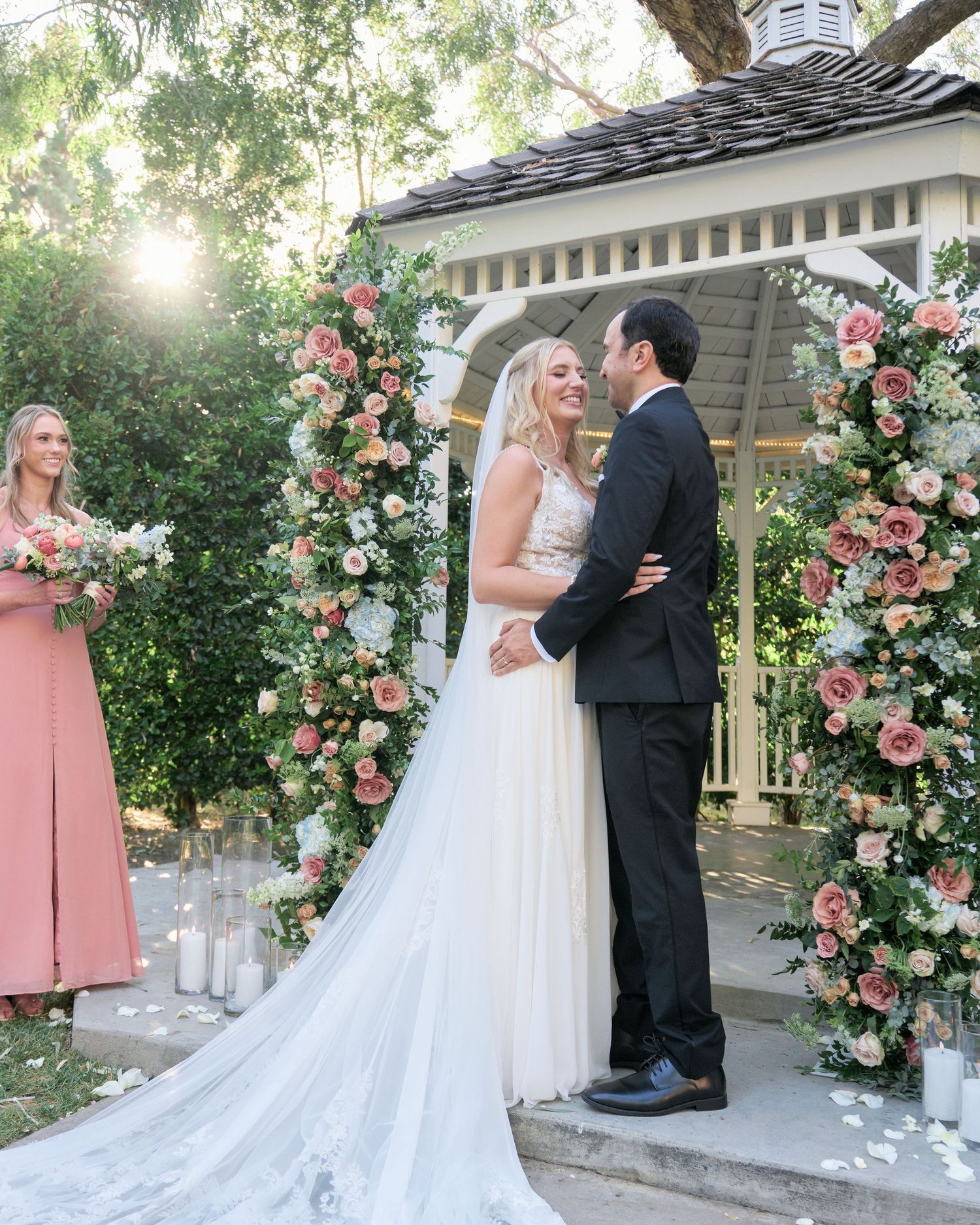 Wedding ceremony in a garden gazebo decorated with pink and white floral arrangements.