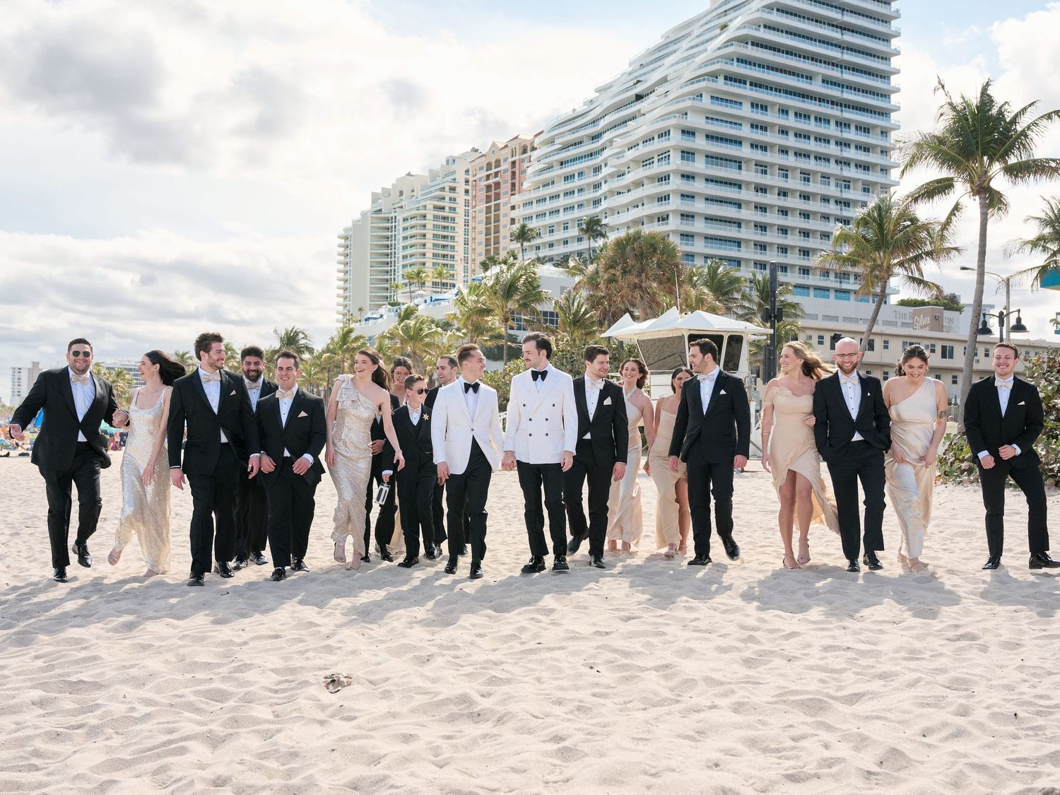 Wedding party poses together on a beach with modern coastal buildings in the background.
