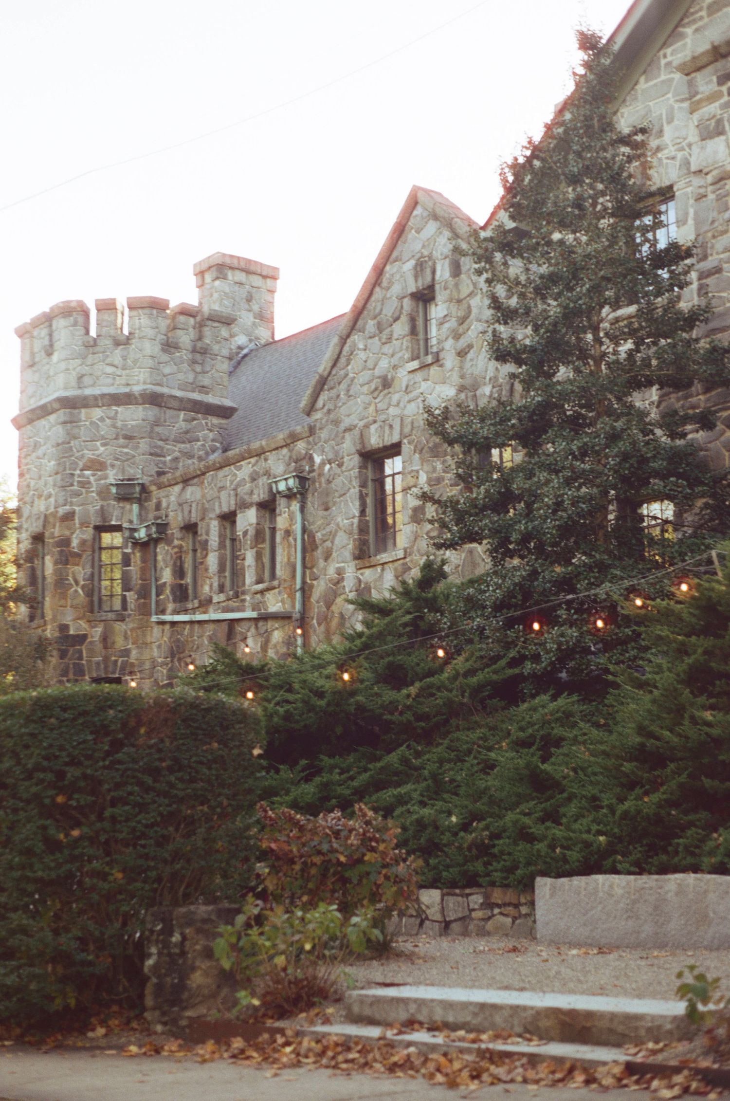 Stone castle-style building with turrets and windows decorated with Christmas lights in autumn setting.