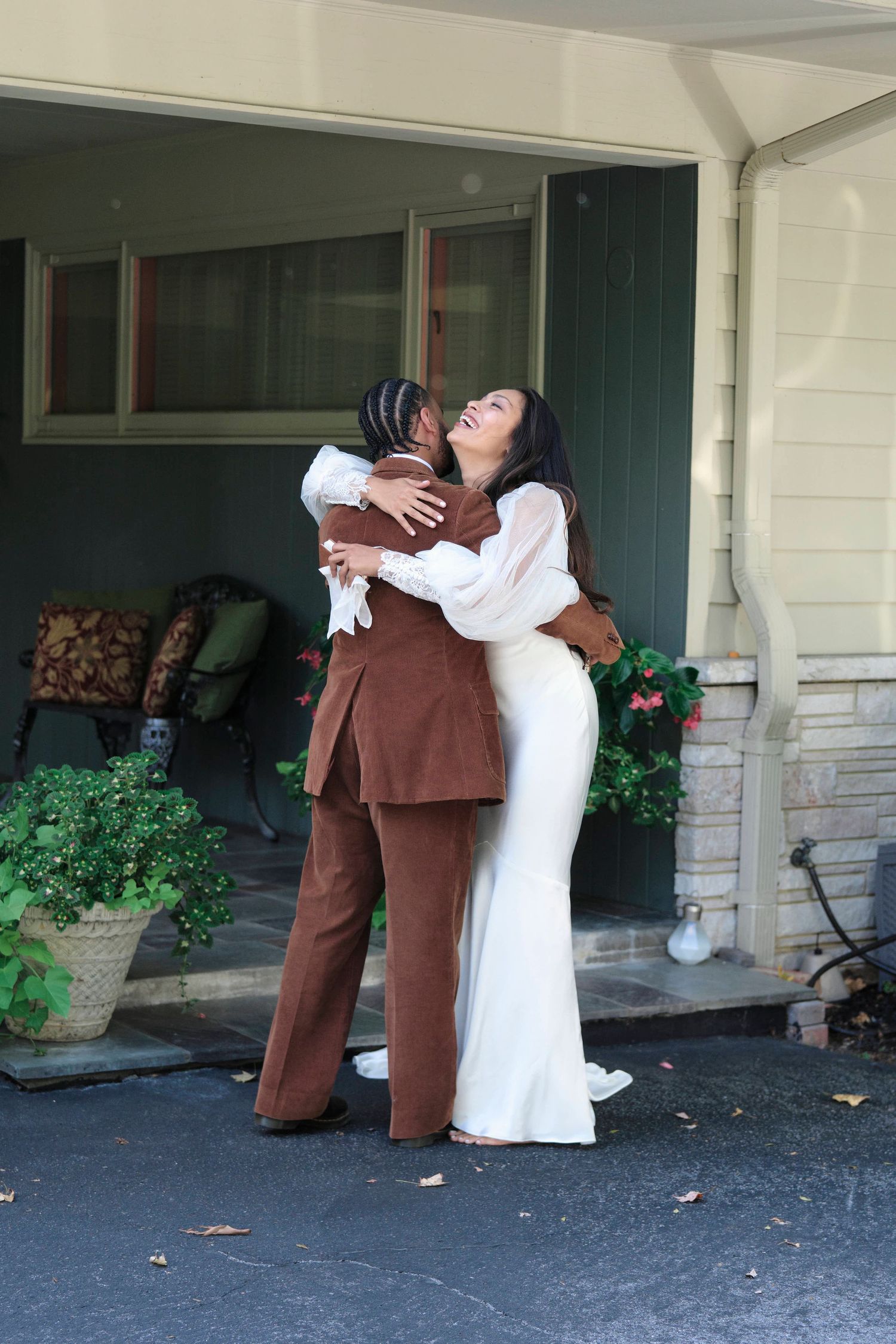 Bride and groom smiling and hugging during their first look in front of a house.