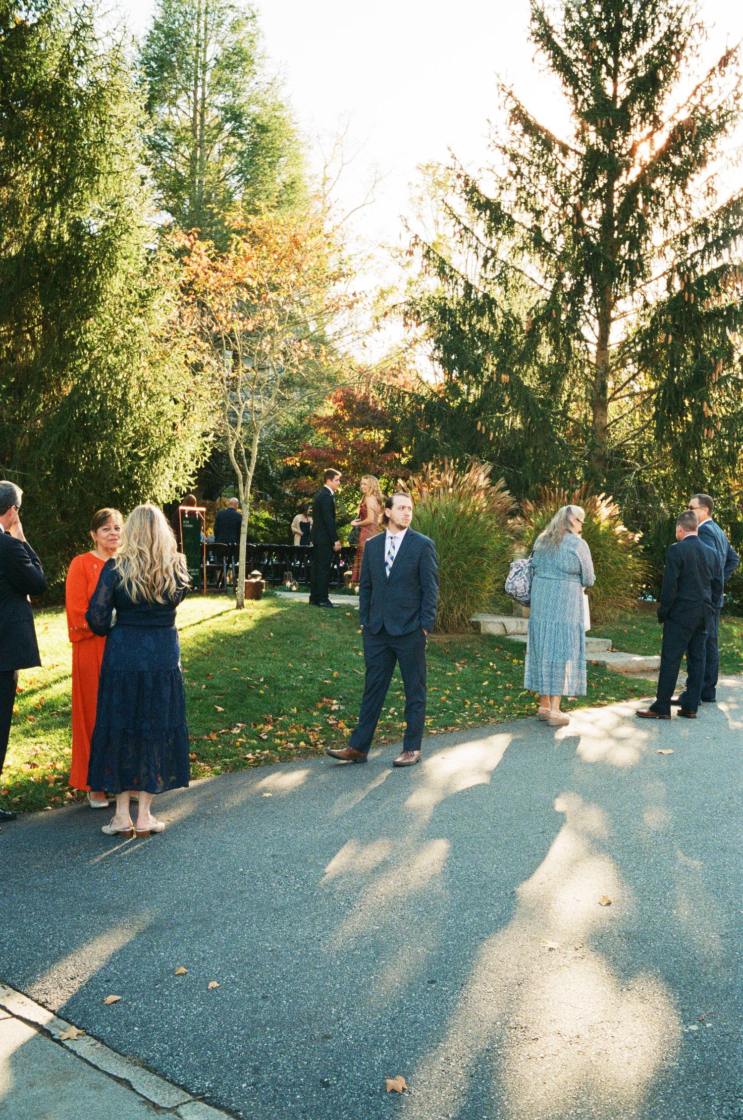 Wedding guests mingling at an outdoor reception with fall foliage in the background.