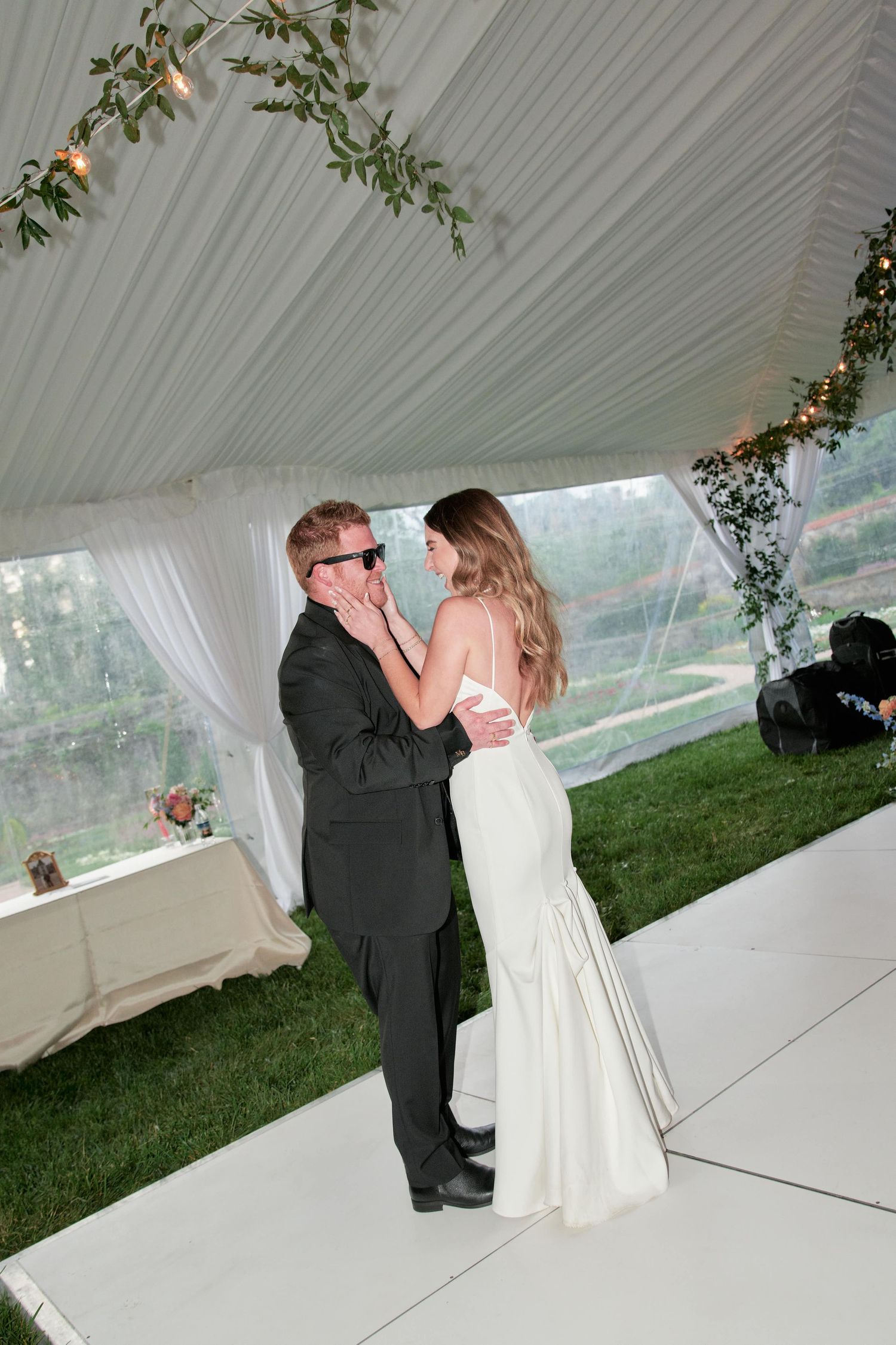 A romantic first dance sequence between newlyweds under an elegant white tent at an outdoor wedding reception.