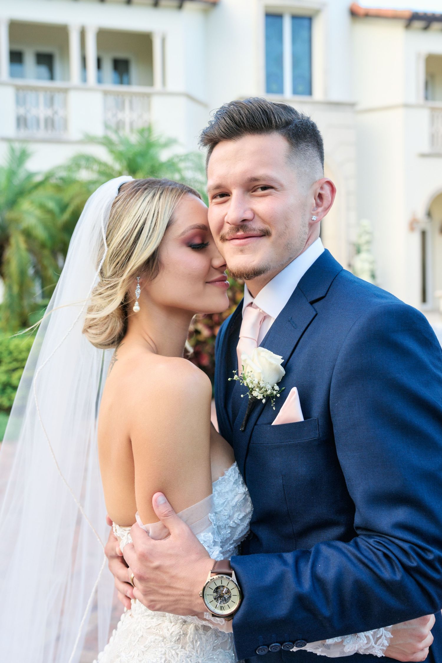 Elegant wedding portrait with couple embracing against white Mediterranean architecture.