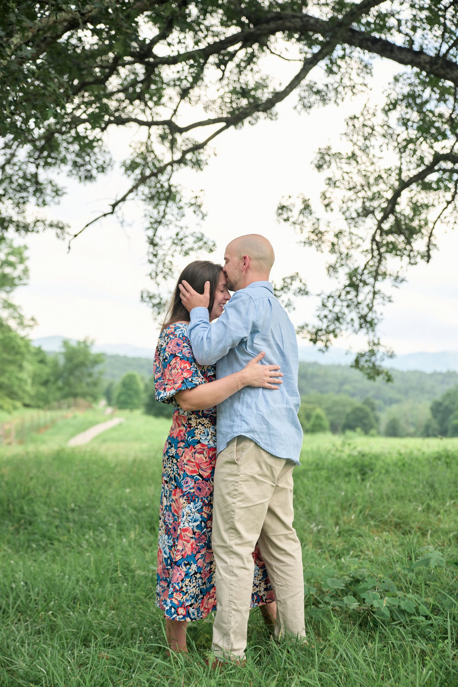 Loving couple embracing under tree branches in scenic mountainside setting.