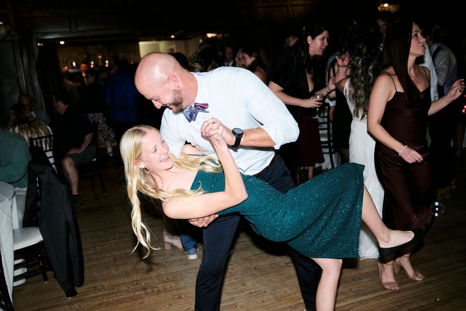 A couple performs a dramatic dance dip move during a wedding reception.