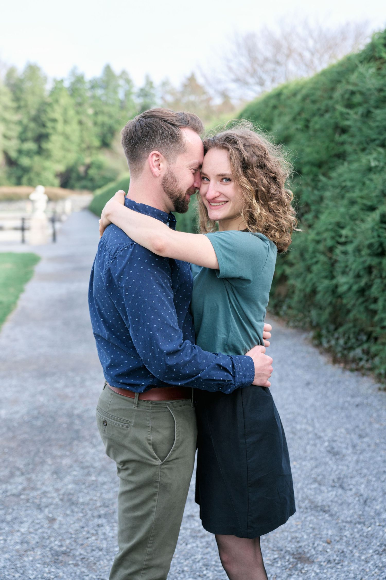 Romantic couple embracing on garden path surrounded by manicured hedges.