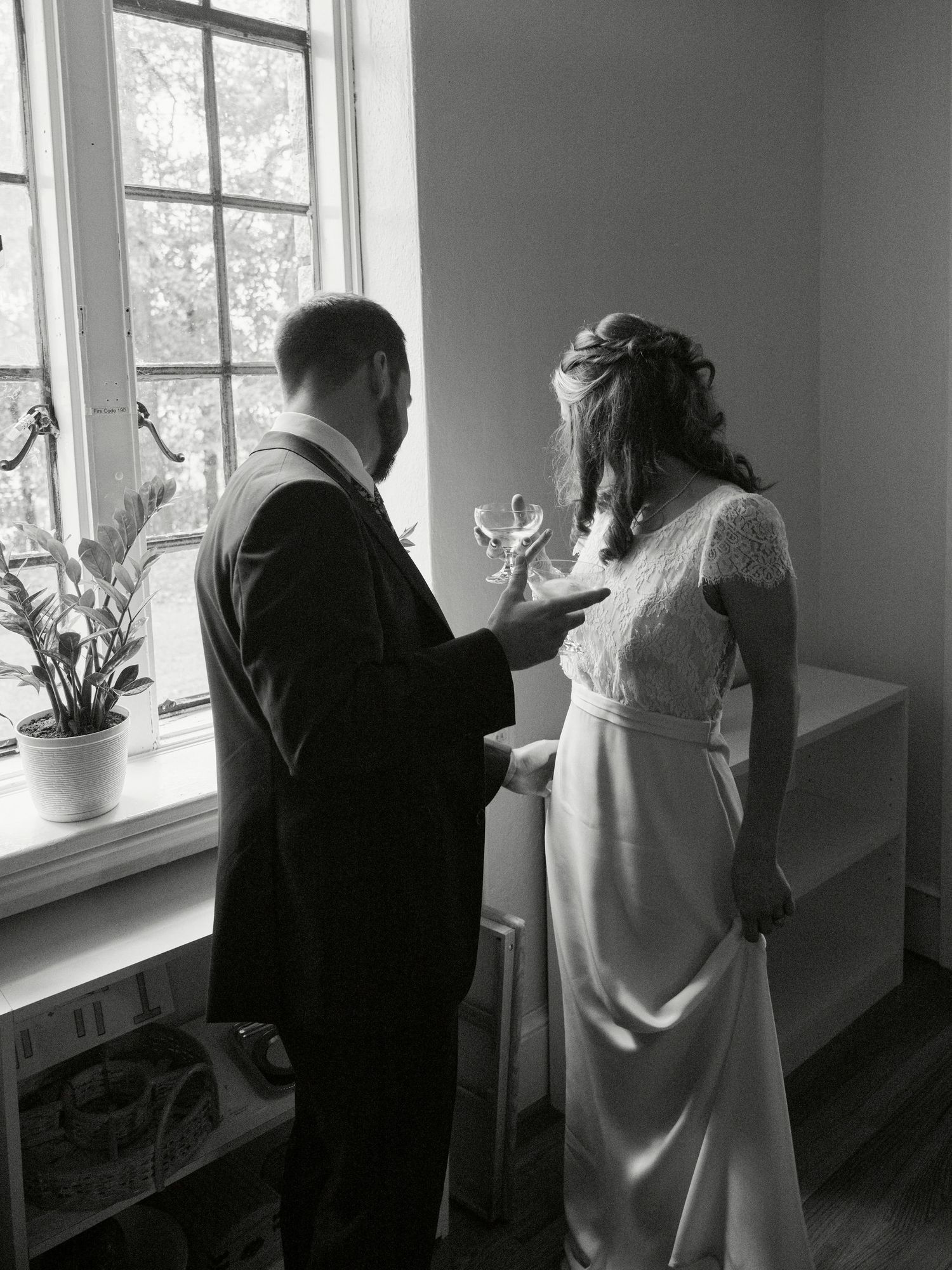 An intimate black and white moment shared by a window during wedding preparations.