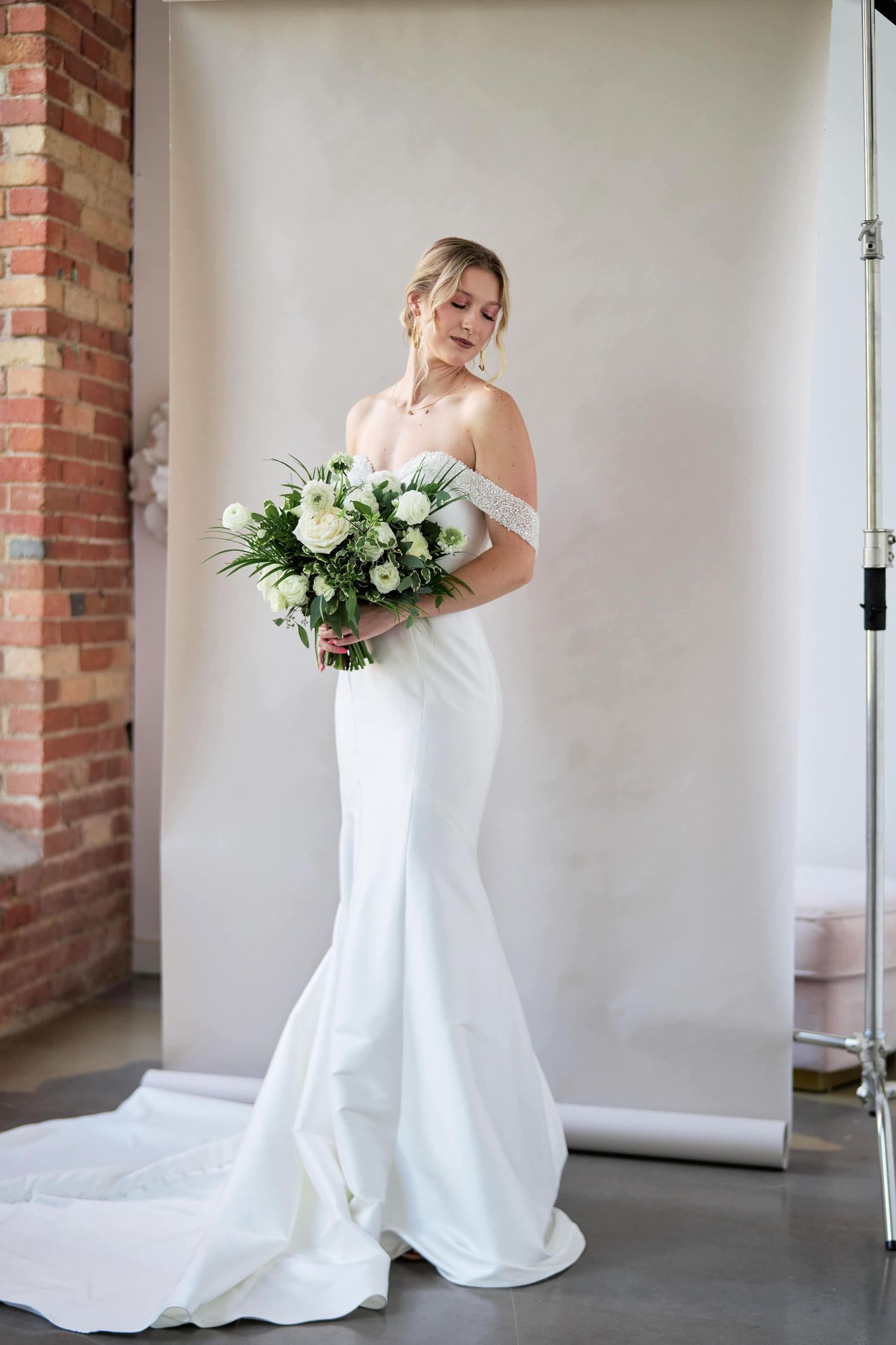 Bride poses in fitted white mermaid wedding dress with off-shoulder detail and trailing train.