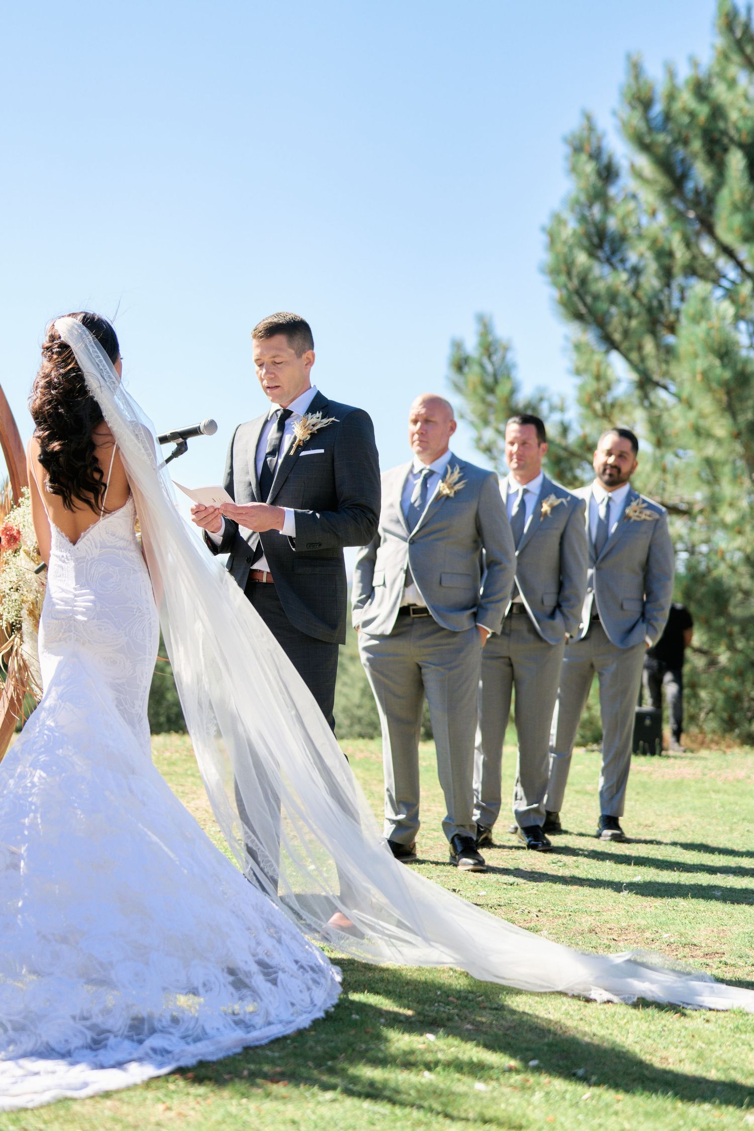 Outdoor wedding ceremony with bridal party in gray suits standing in line during the vows.