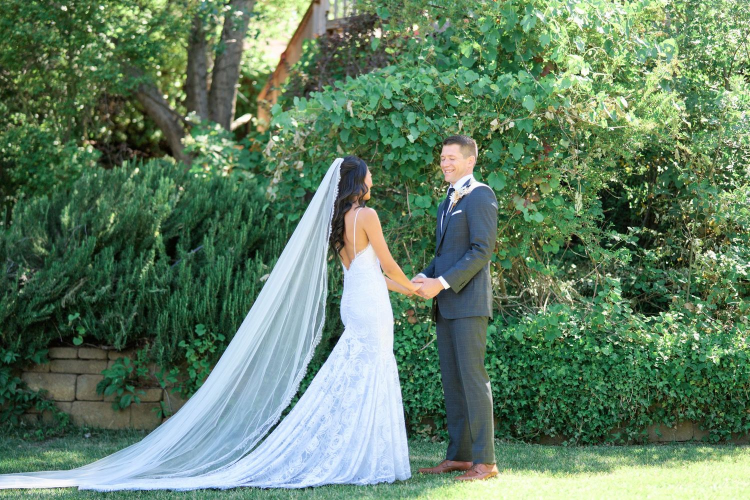 A couple holding hands during their garden wedding ceremony surrounded by greenery.