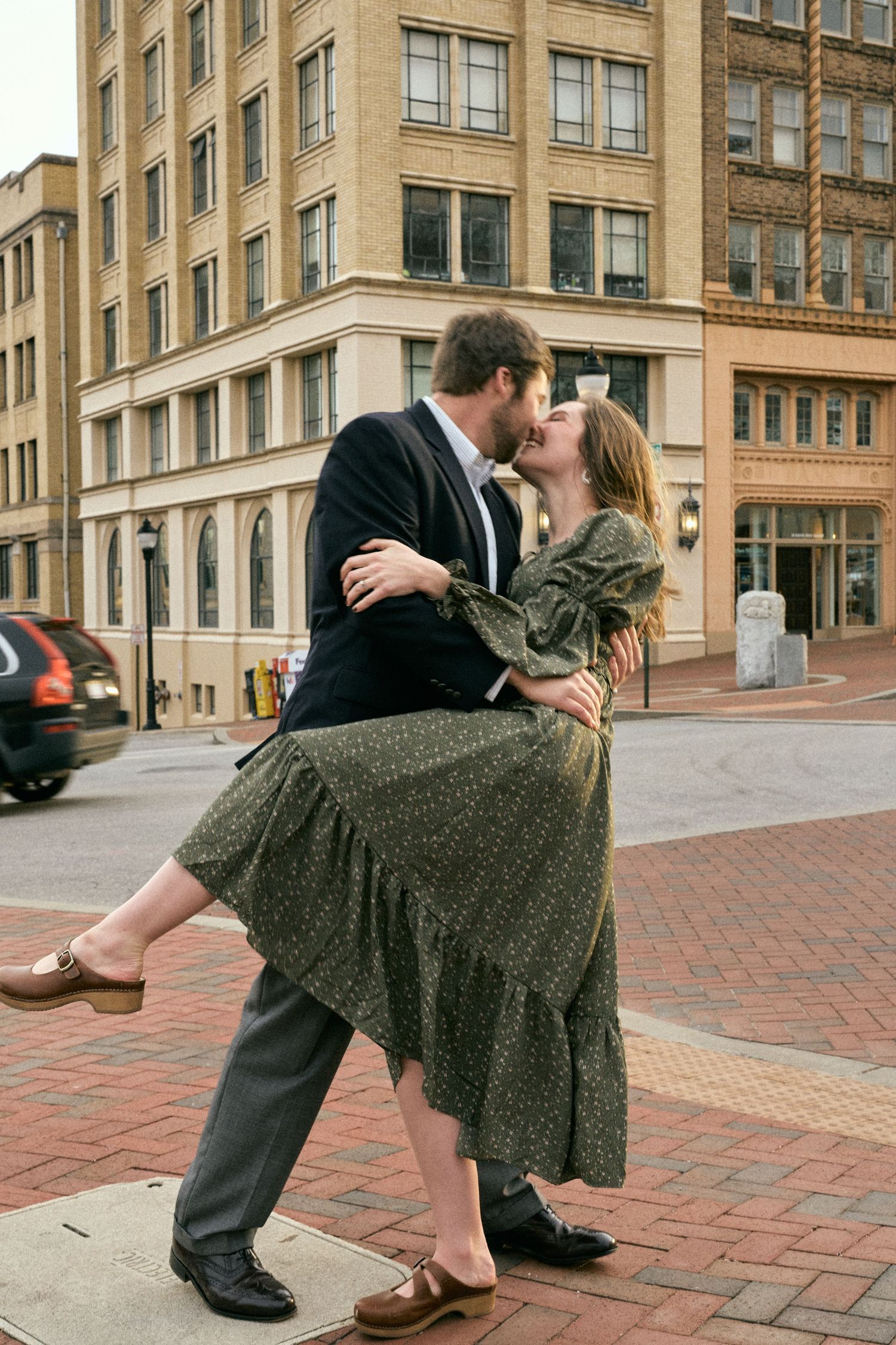 A romantic dance dip pose on a brick sidewalk in front of an urban building.