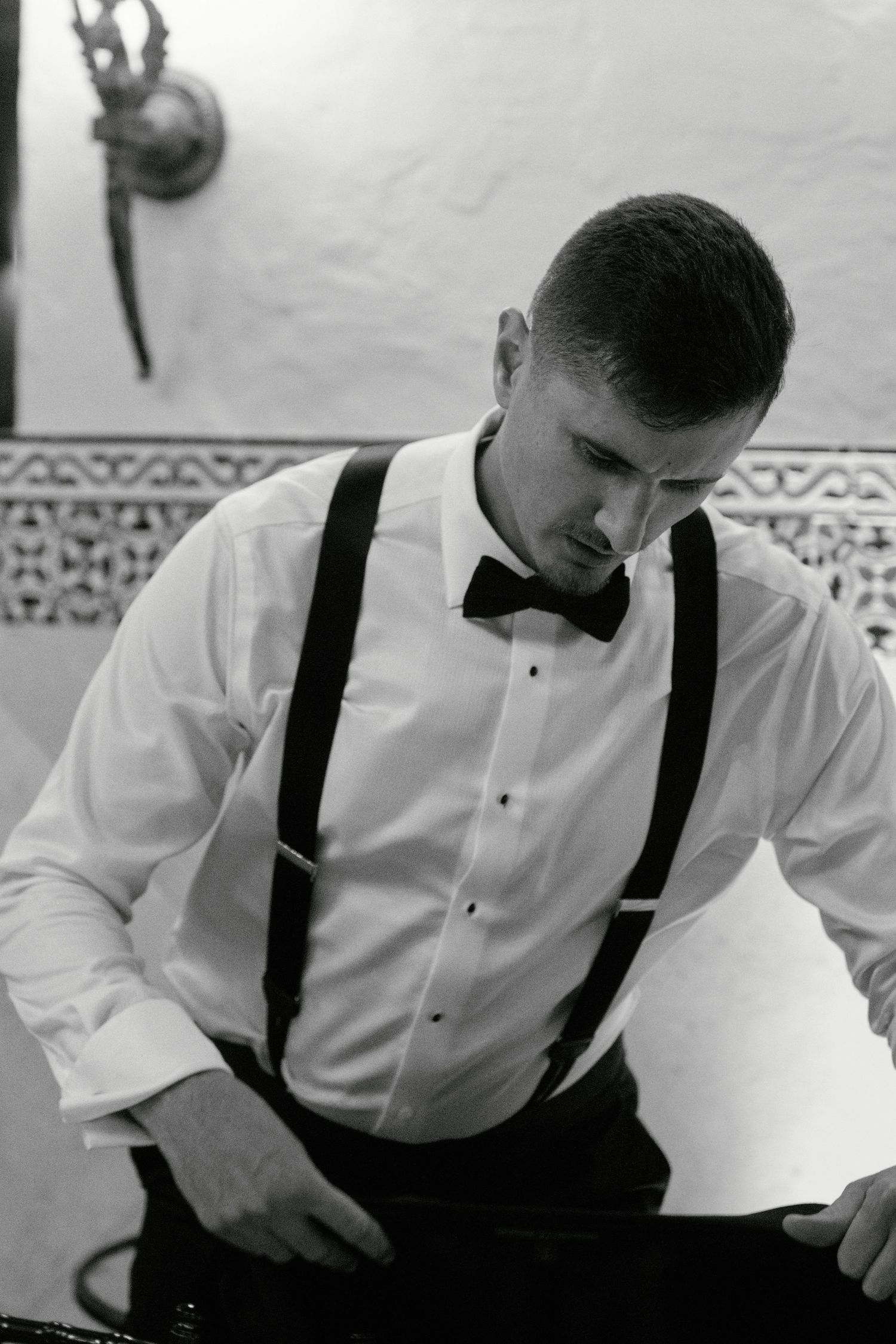 Groom in classic white shirt and suspenders adjusts his bowtie.