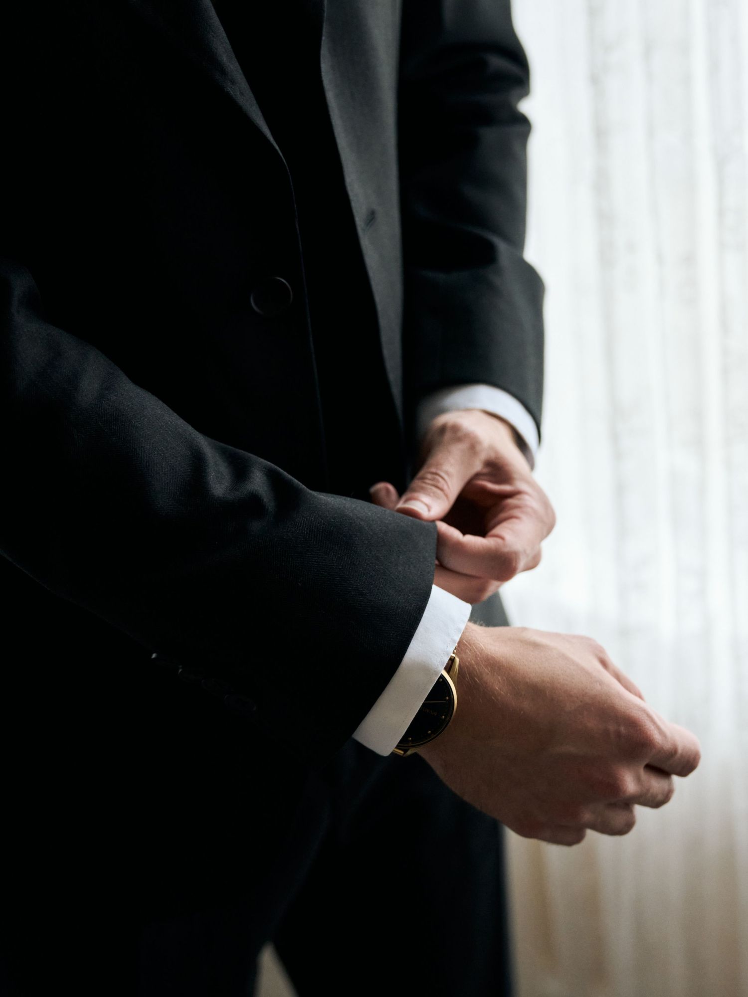 Close-up view of hands adjusting formal suit cuffs against a light background.