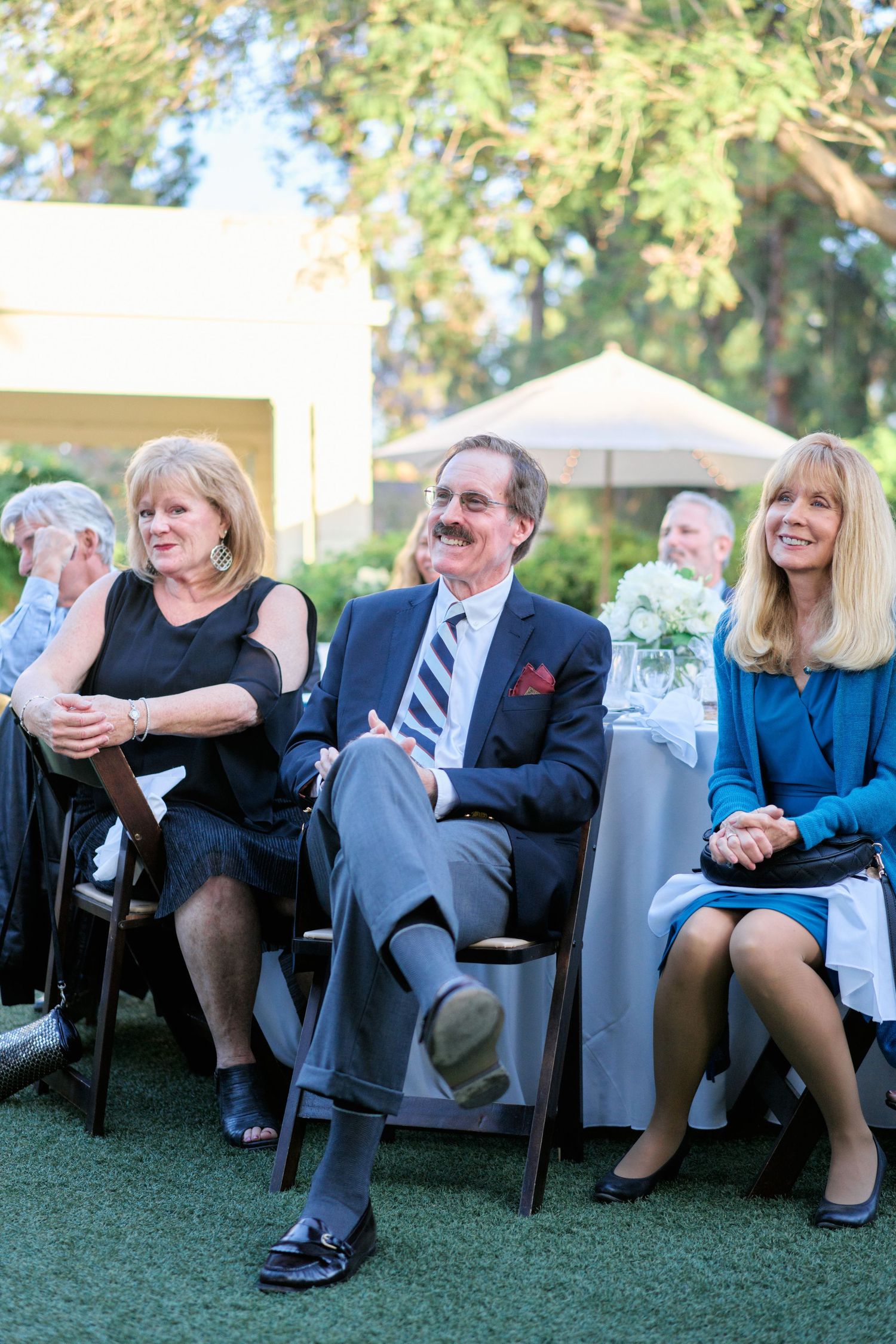 Wedding guests seated on lawn chairs enjoy the outdoor celebration.