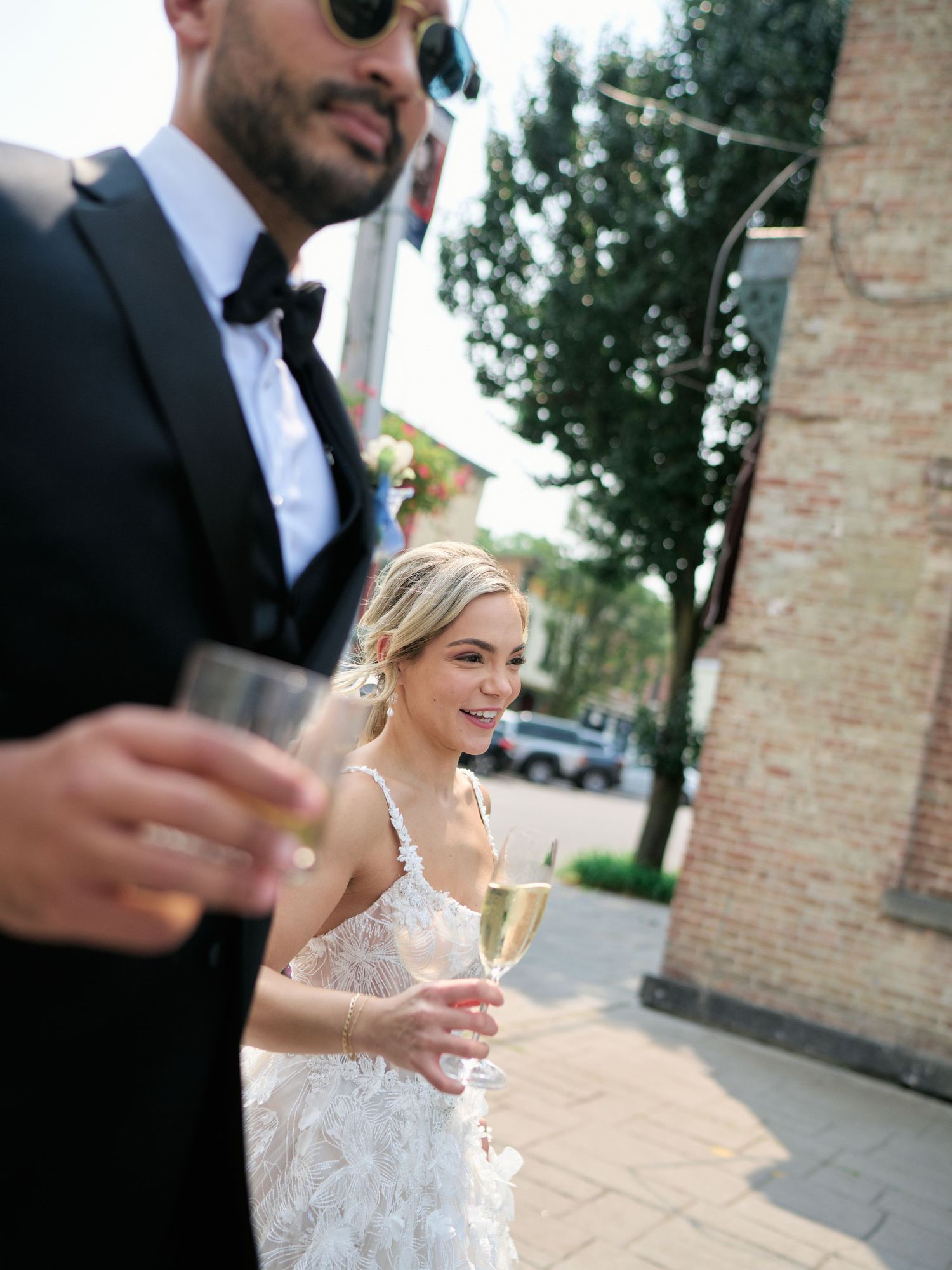 A couple in wedding attire raise champagne glasses during an outdoor celebration.