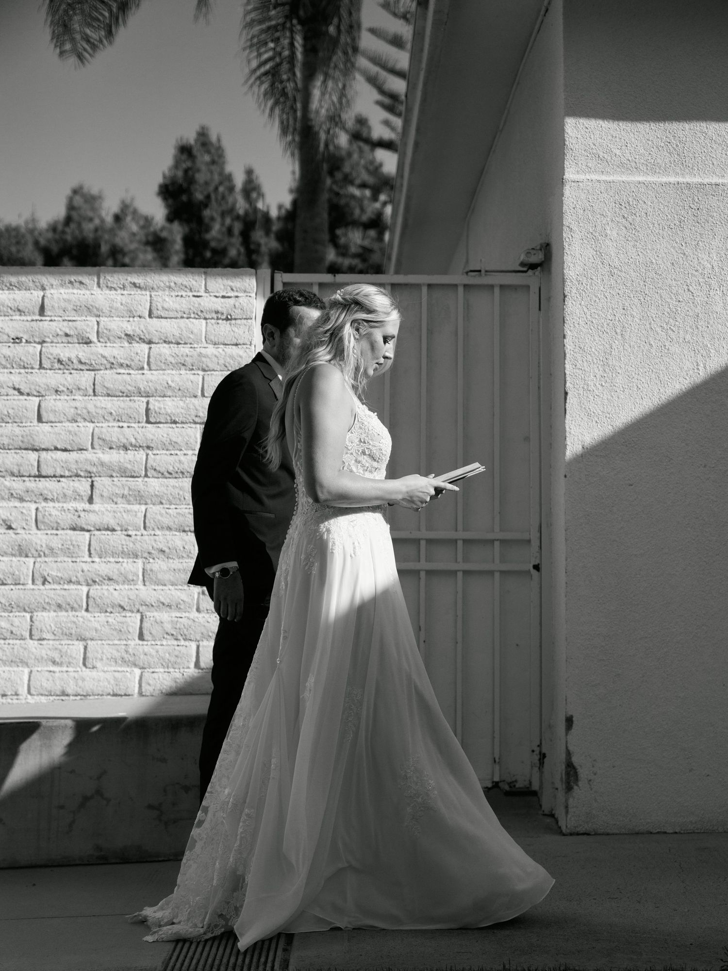 A black and white image of a couple reading together outside against a textured wall.