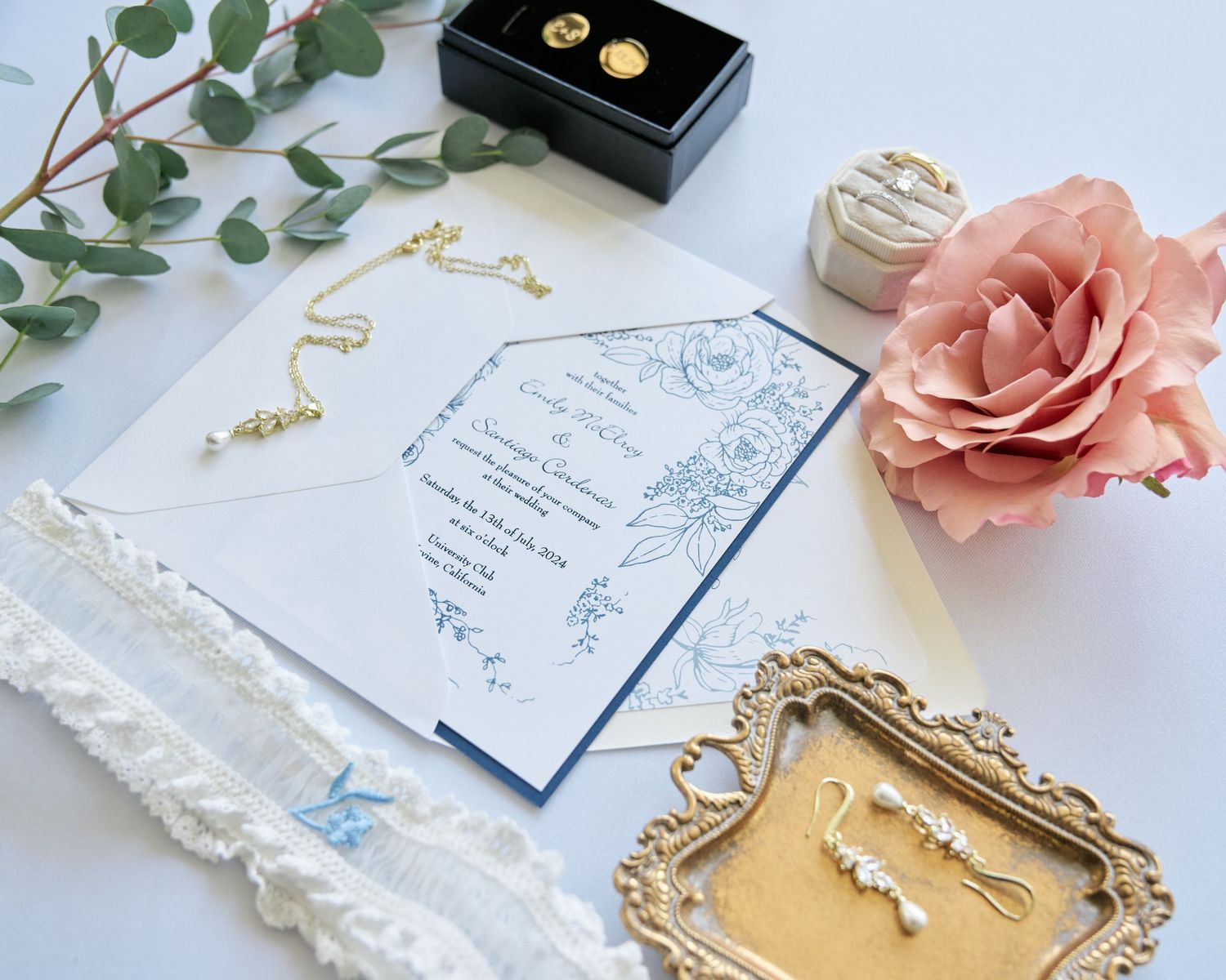 Wedding stationery flat lay with roses, gold jewelry tray, and delicate lace accents.