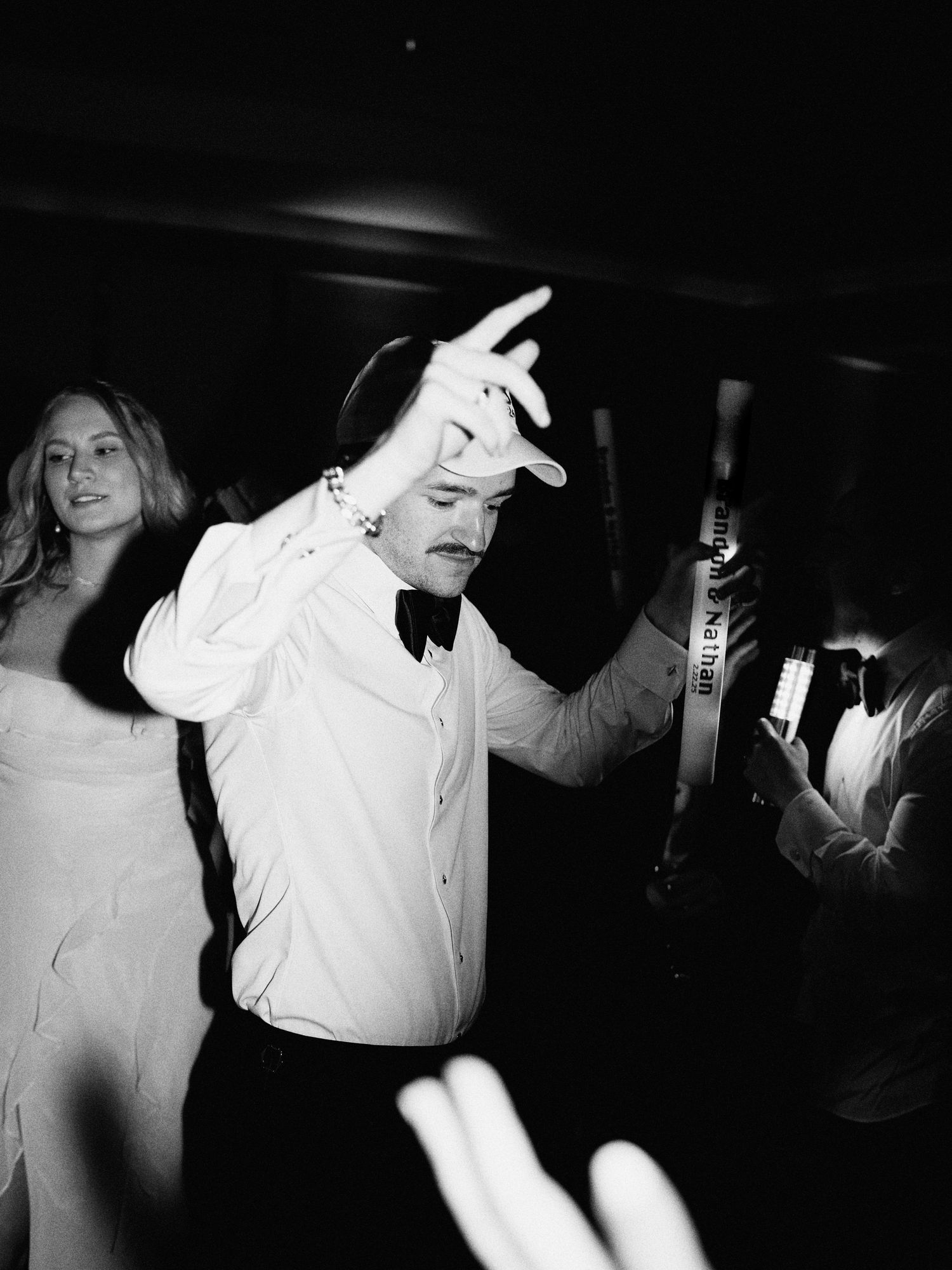 A person in a white dress shirt and bowtie dances energetically with raised hands at a dark party venue.