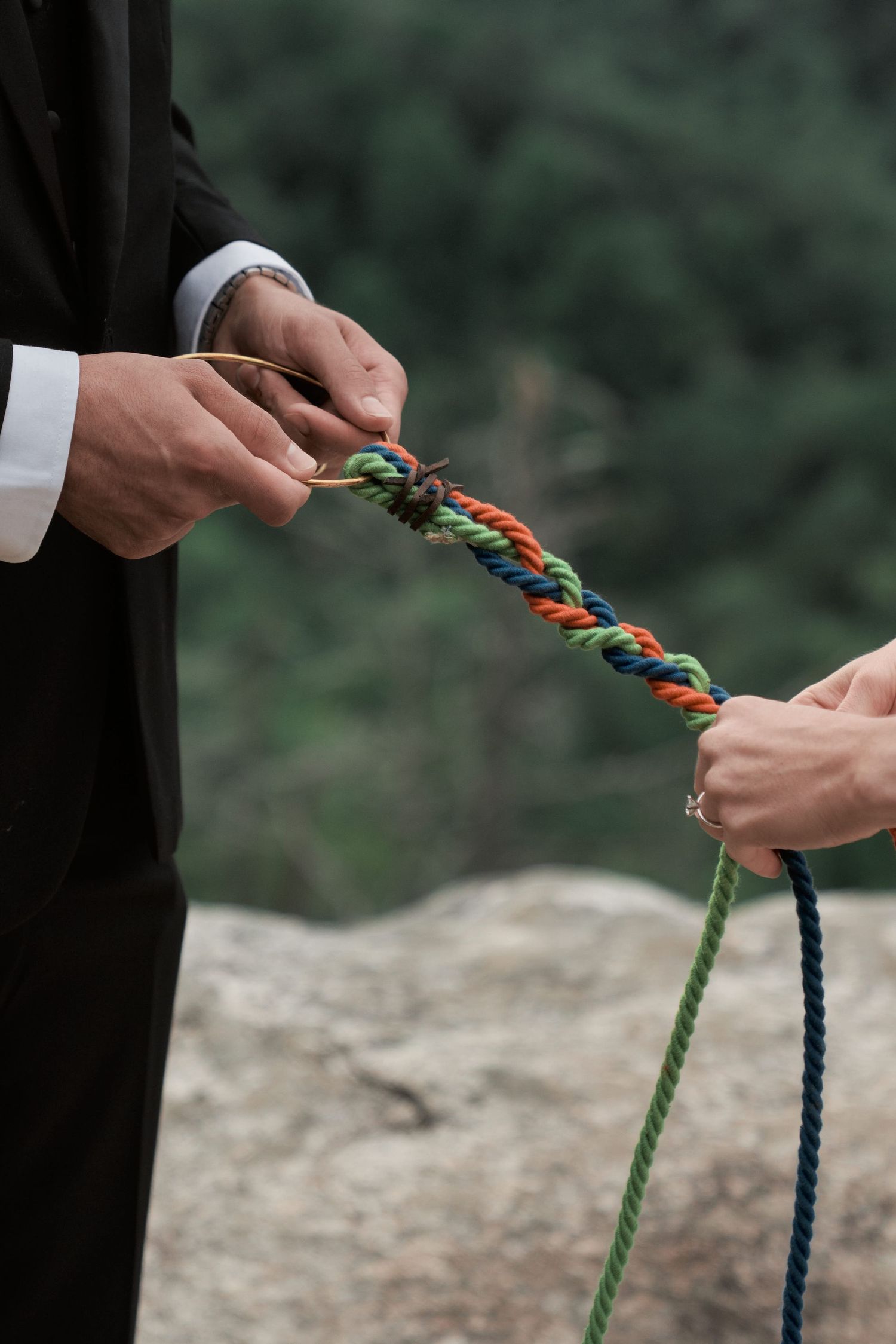 Close-up of hands tying together blue and green ropes in an outdoor setting.