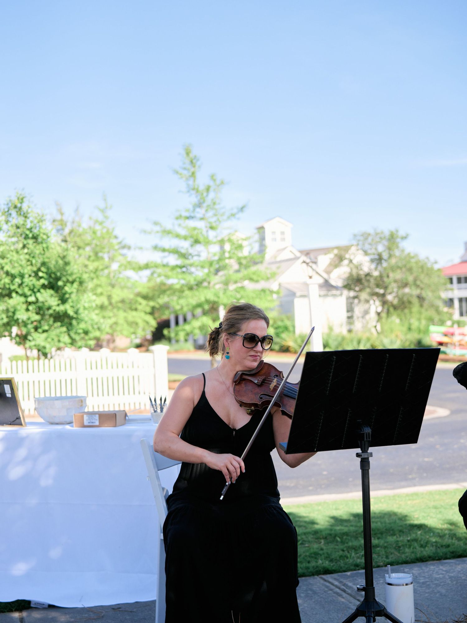 Professional violinist in a black dress performs outdoors on a patio with a music stand during a summer event.