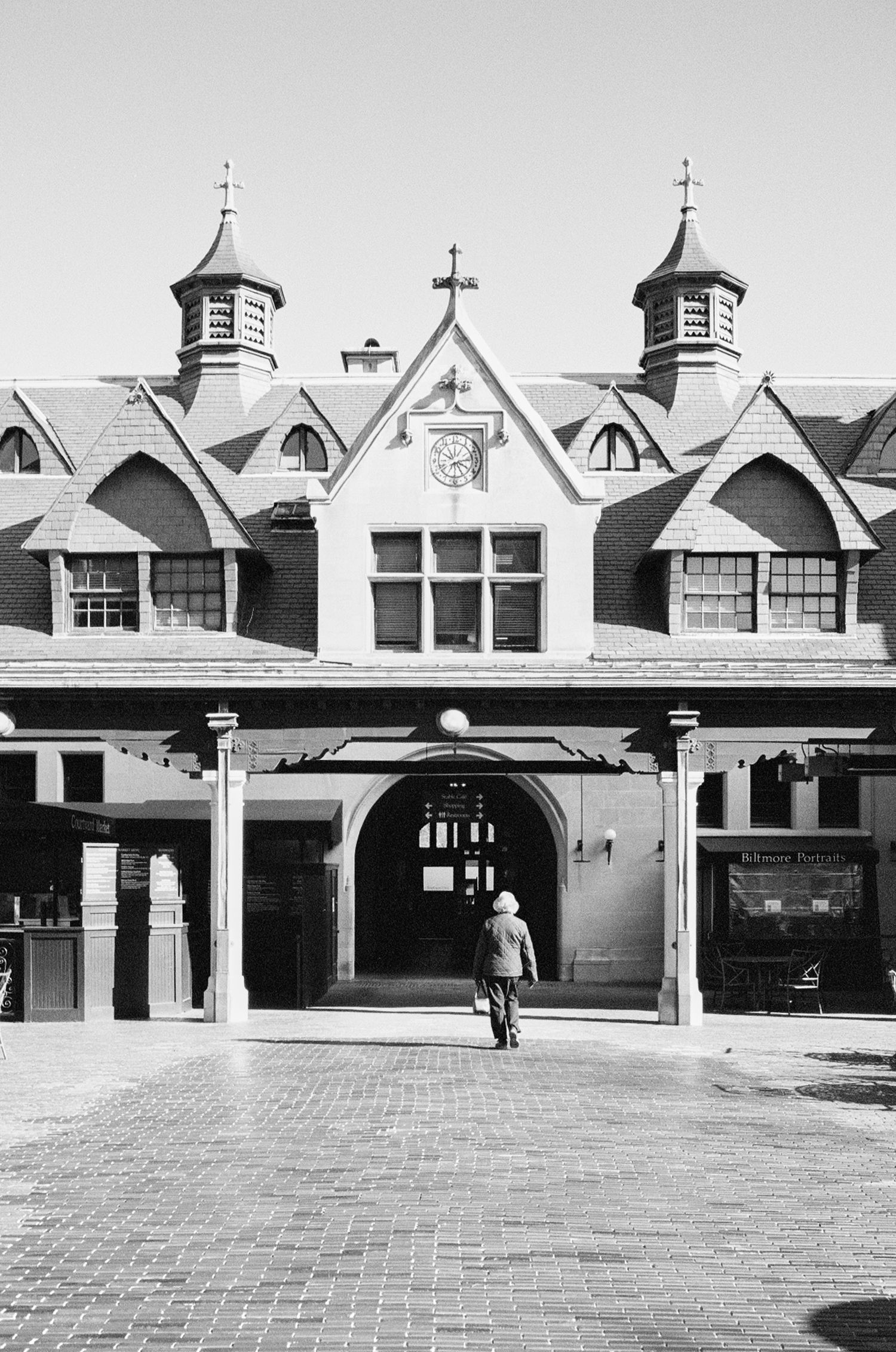 Historic black and white photograph of an ornate building entrance with twin cupolas and dormer windows from early 1900s.