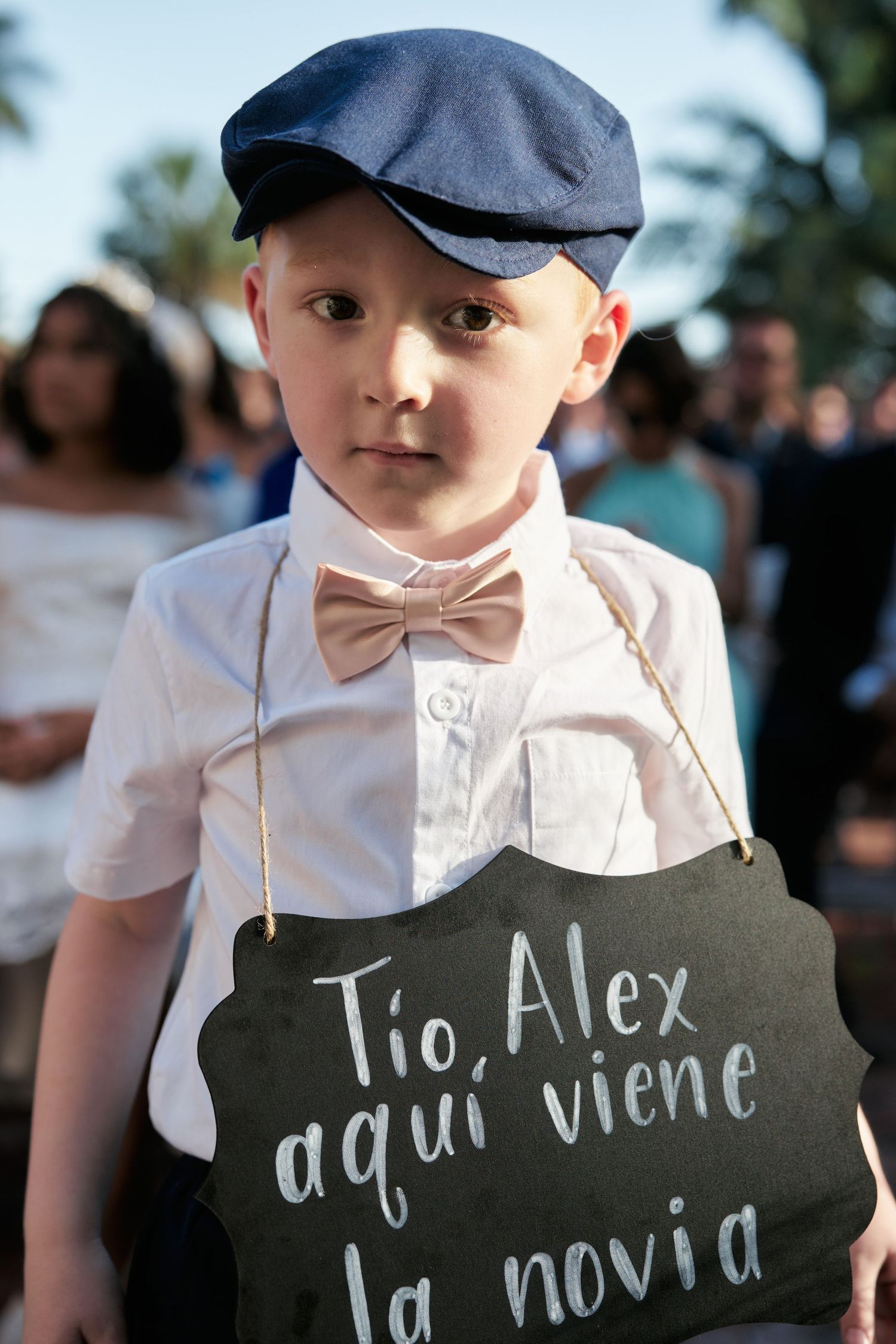 Young ring bearer in formal attire holding a chalkboard sign in Spanish at a wedding.
