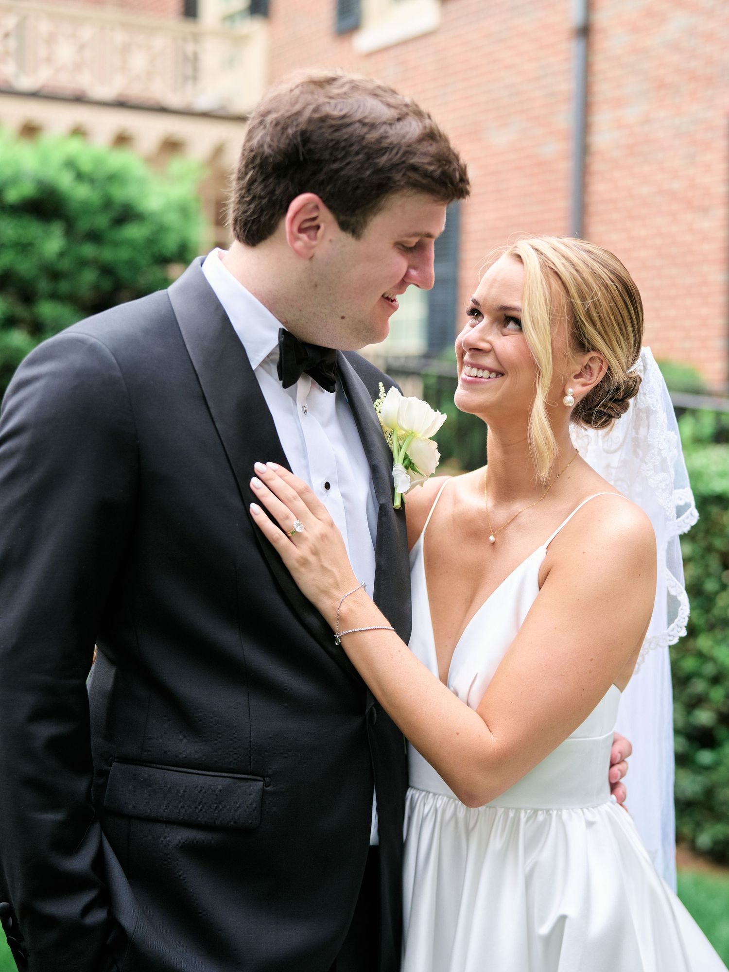 A romantic wedding portrait of a couple in formal attire sharing an intimate moment against a brick building.