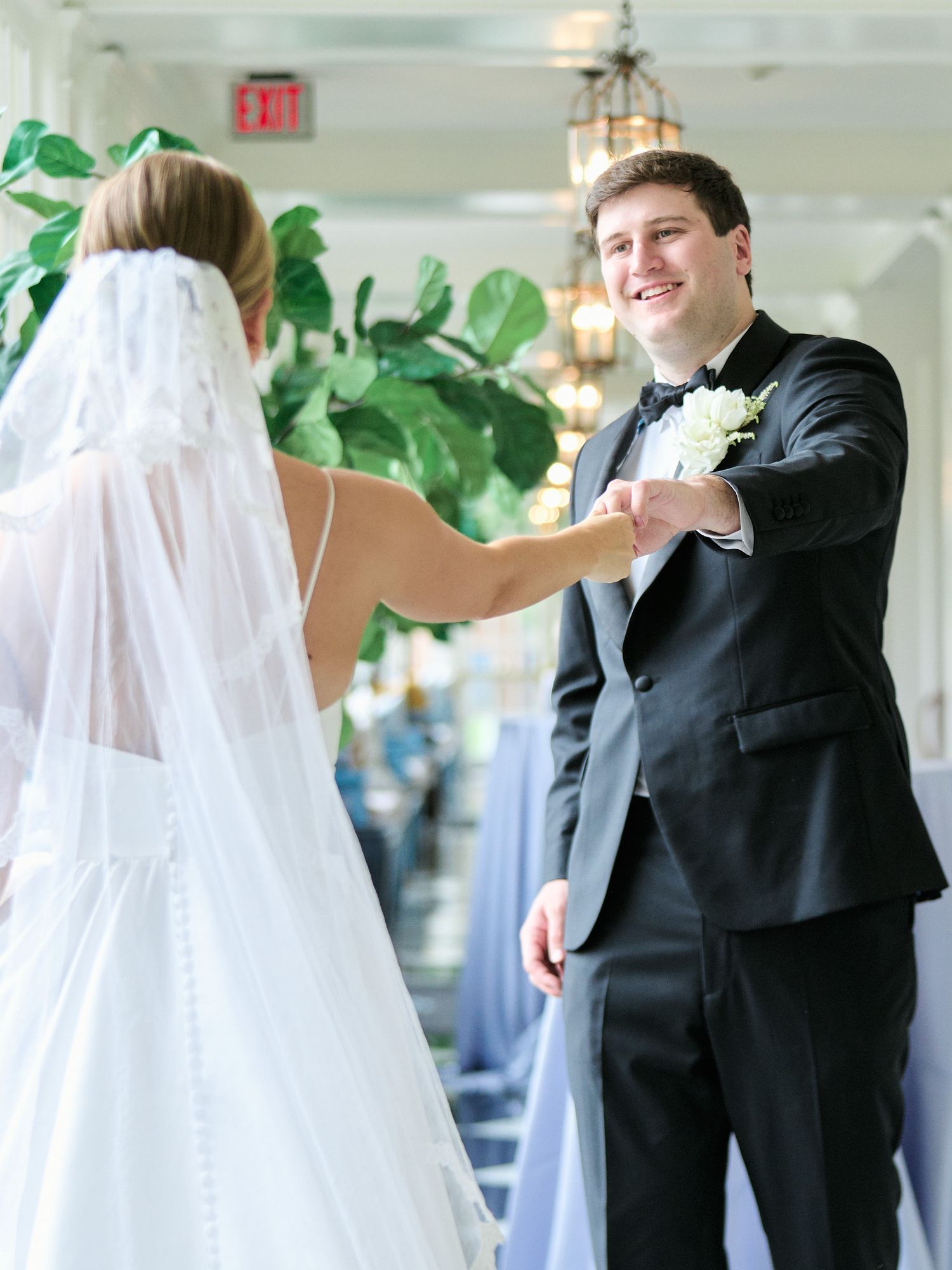 Couple shares first dance in elegant venue hallway with hanging lanterns and greenery.