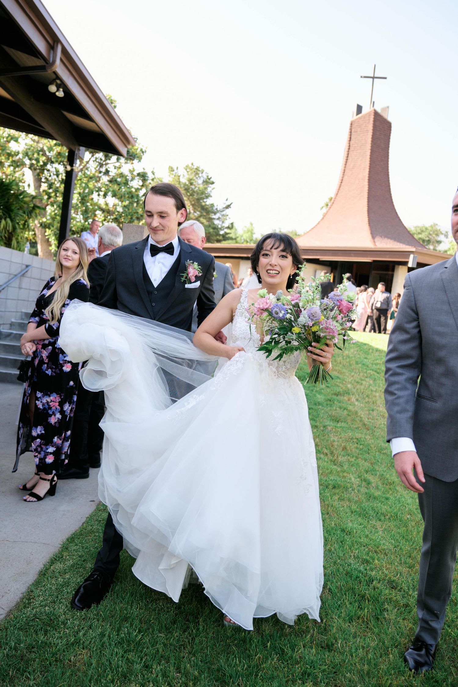A joyful wedding couple exit their ceremony at a church with a distinctive cross.