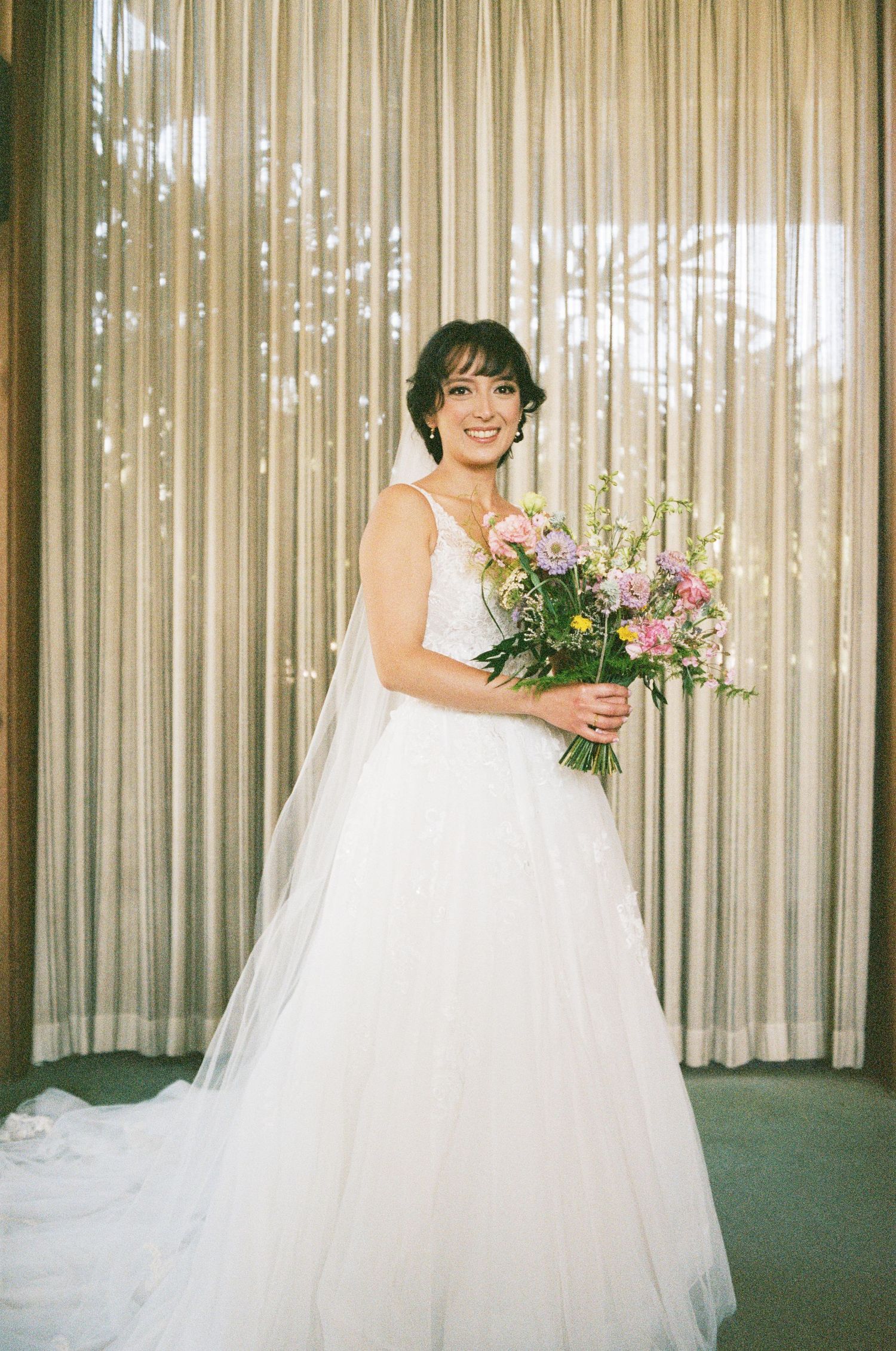 Radiant bride in white flowing gown holding colorful spring bouquet.