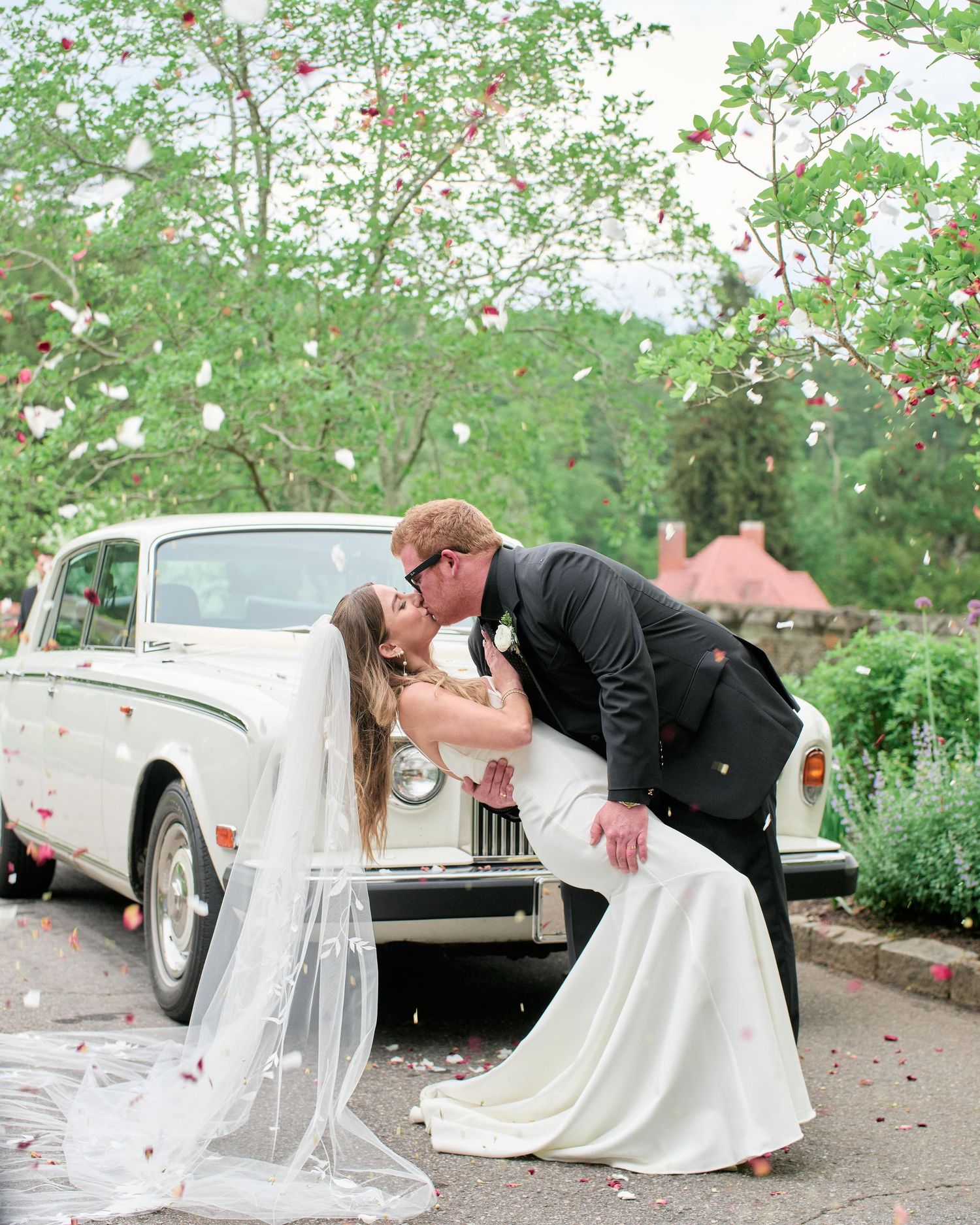A romantic sequence of wedding photos showing a couple dipping and posing near a classic vintage car in a garden setting.