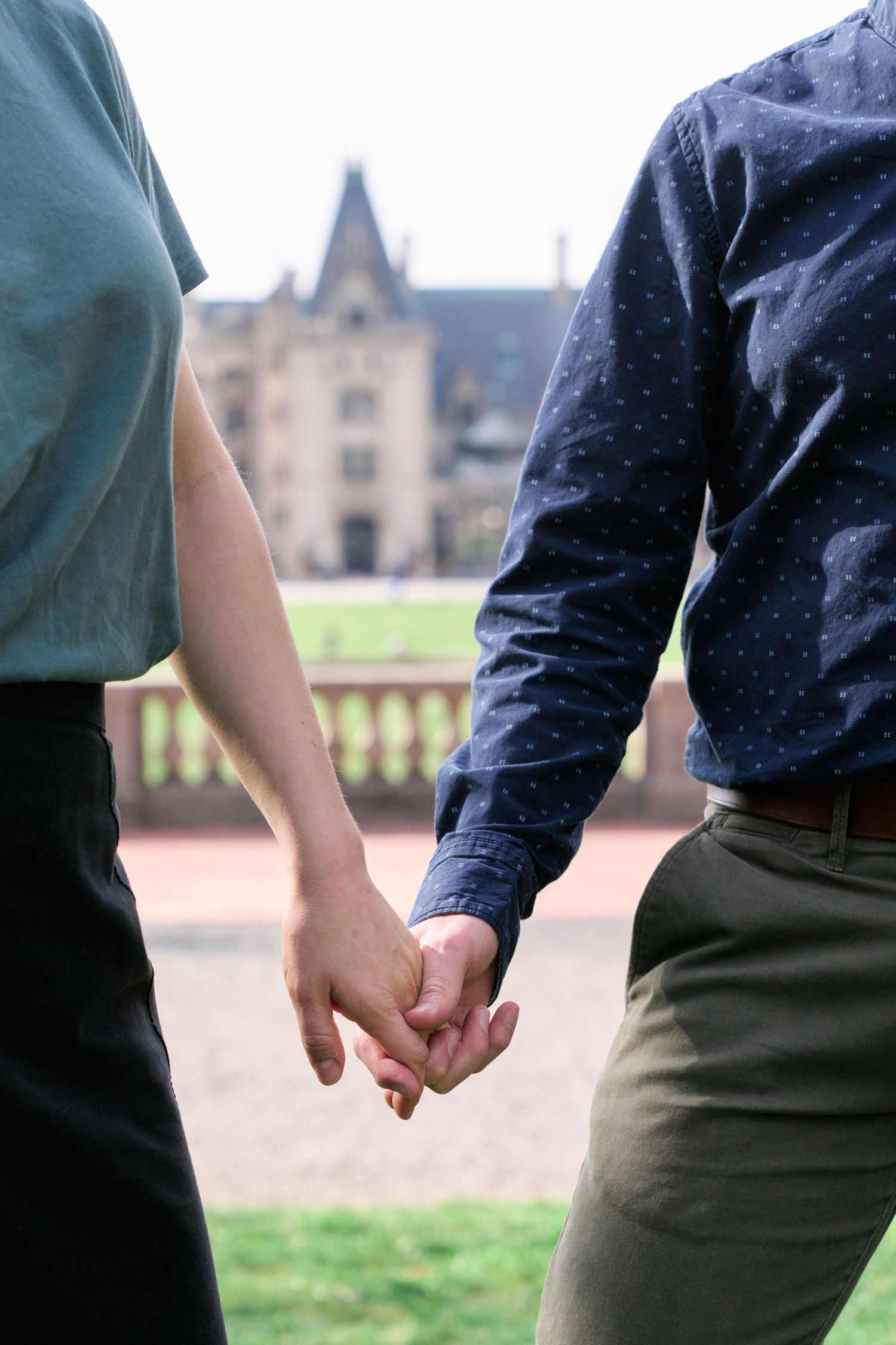 Detail photos of couple holding hand with the Biltmore House in the background.