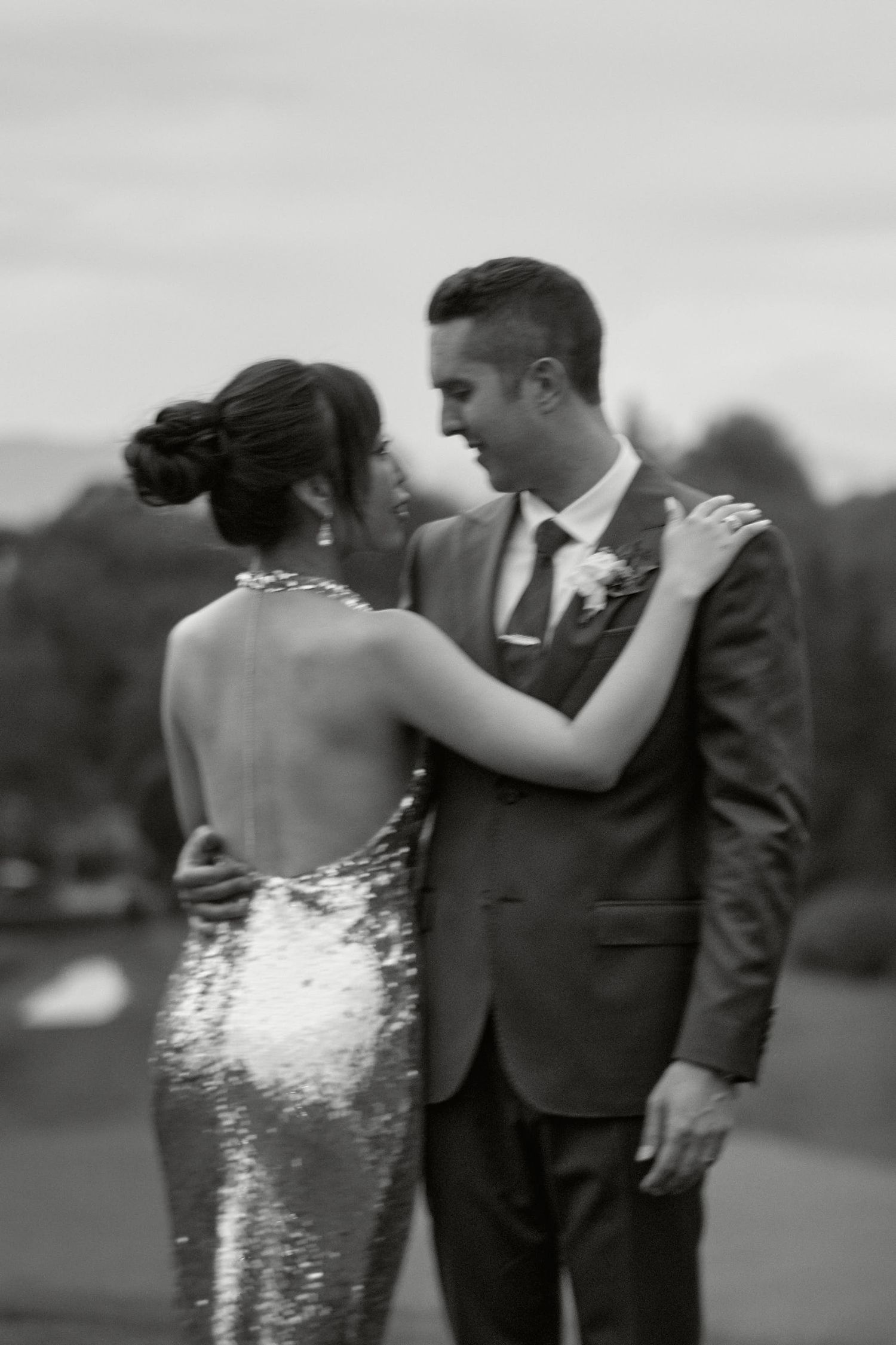 A black and white portrait of a couple in formal attire sharing an intimate moment outdoors.