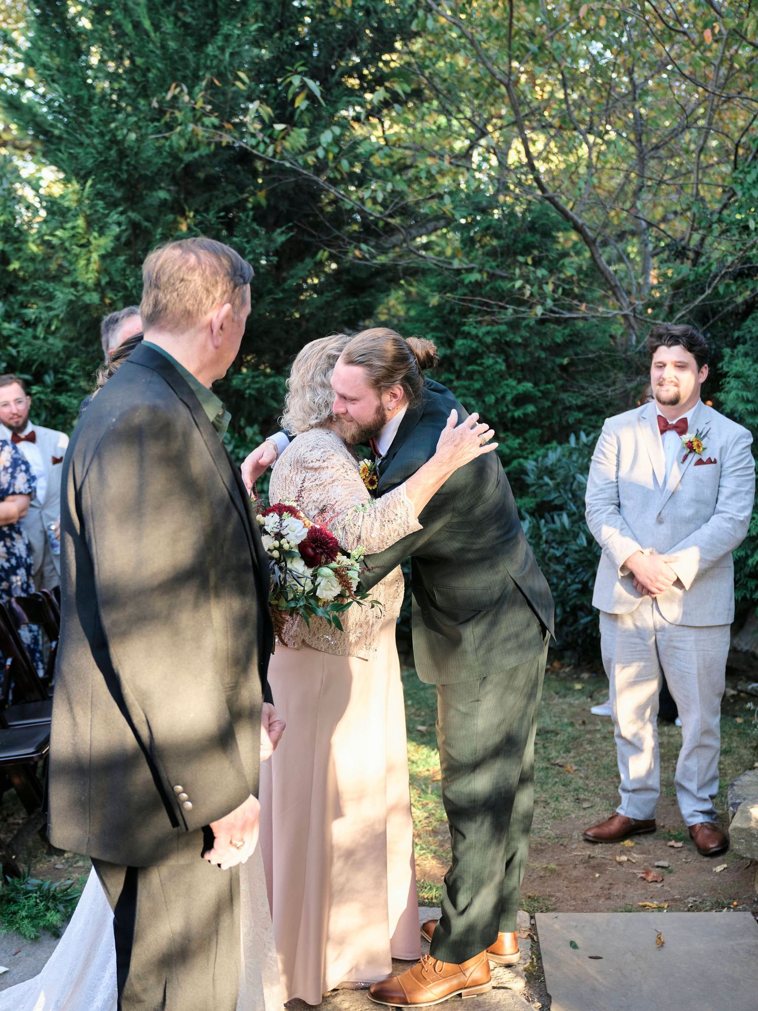 A wedding ceremony moment captured outdoors with attendees in formal attire surrounded by natural greenery.
