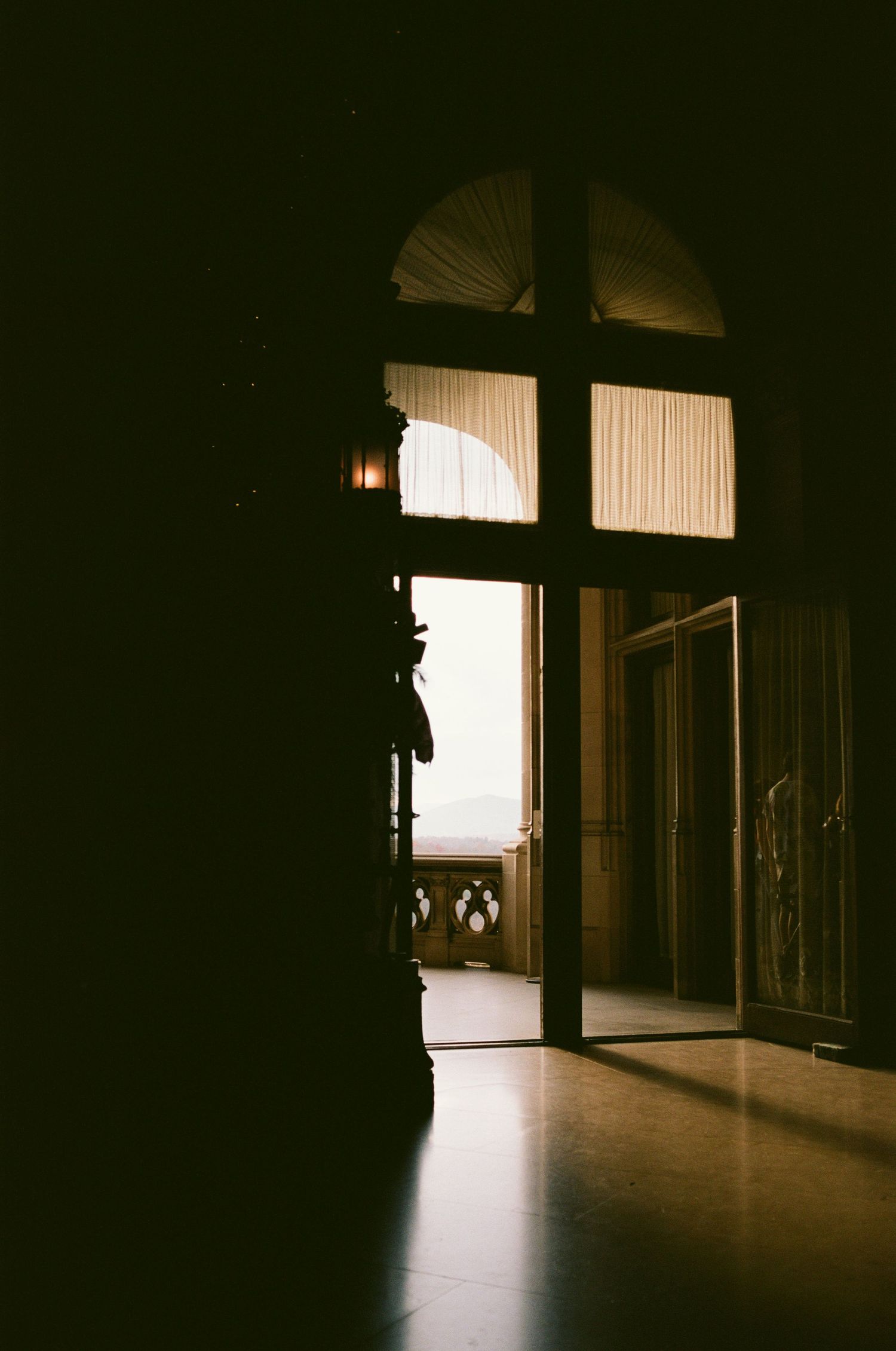 Dramatic doorway with arched window and streaming sunlight in dark hallway.