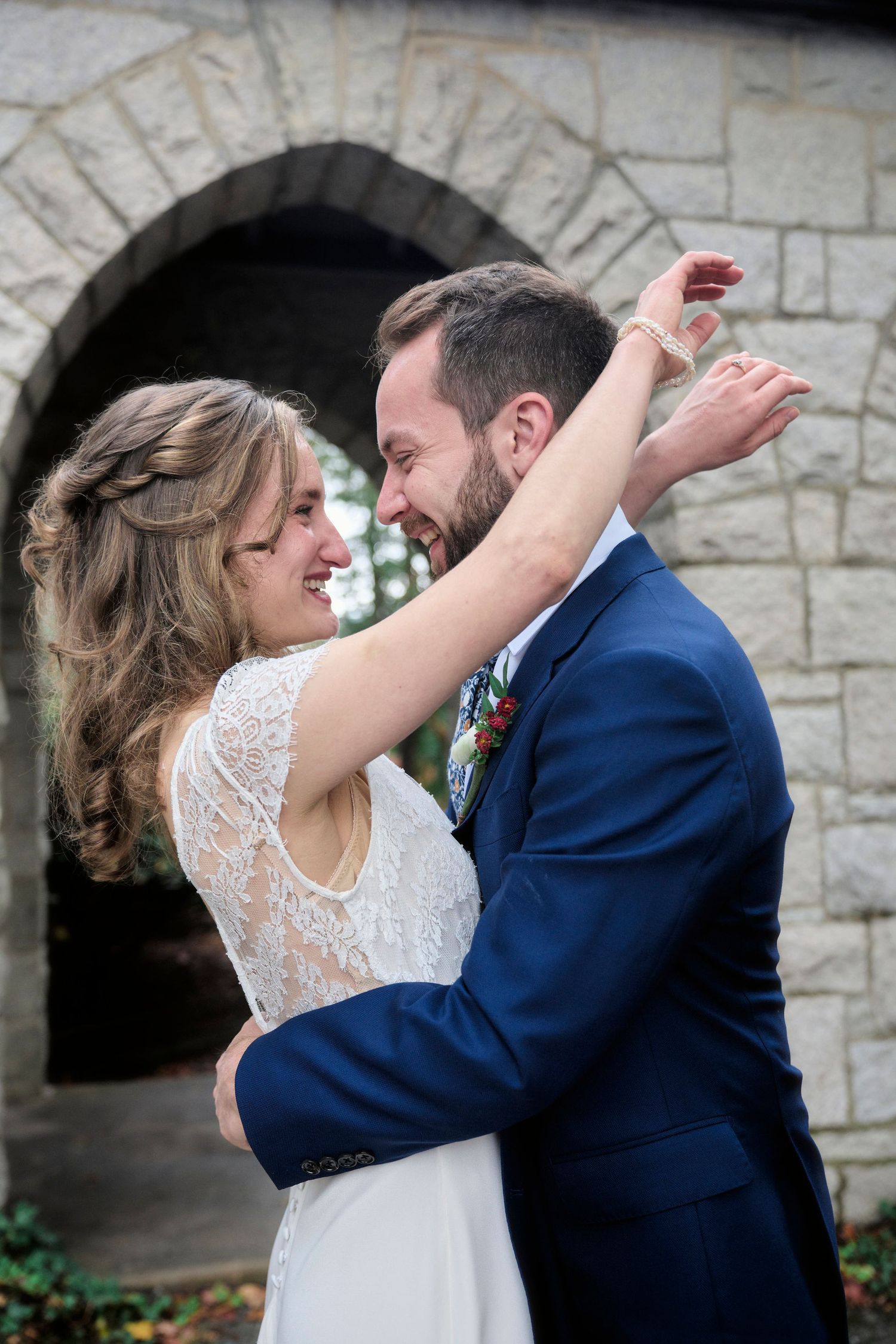 A joyful wedding moment captured as the couple dances and laughs together by a stone church entrance.