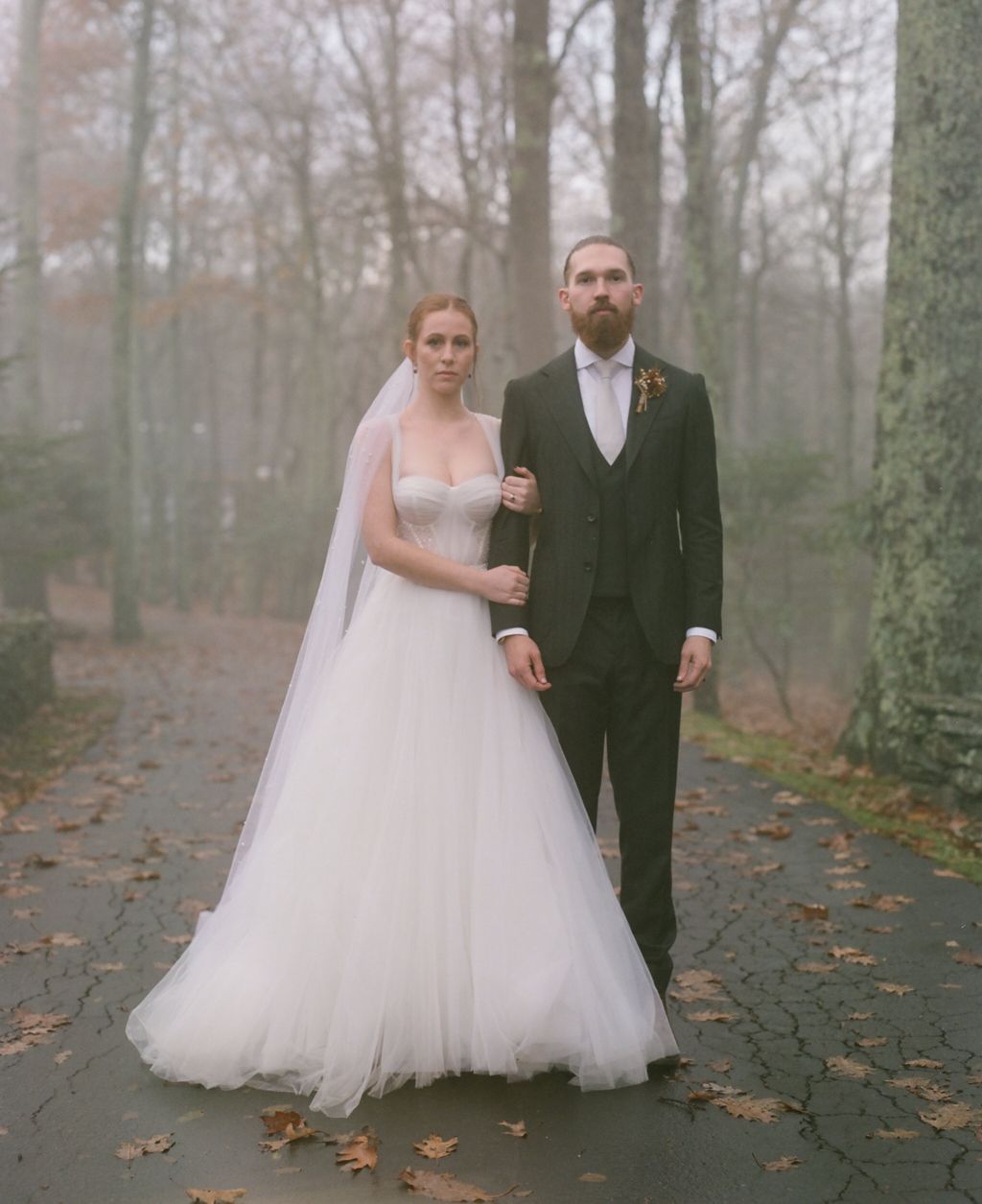 A classic autumn wedding portrait of a couple standing on a misty forest path.